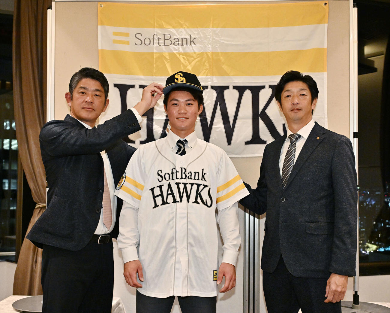 仮契約を終えたソフトバンクドラフト2位神奈川大・庄子は福山アマスカウトチーフ（左）から帽子をかぶせてもらう。右は松本アマスカウト（撮影・滝沢徹郎）