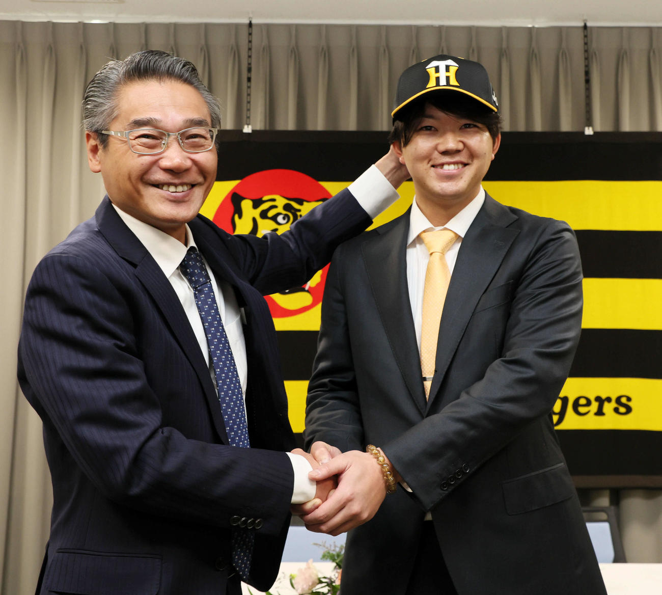 入団会見で嶌村球団本部長（左）から帽子をかぶせてもらう楠本（撮影・加藤哉）