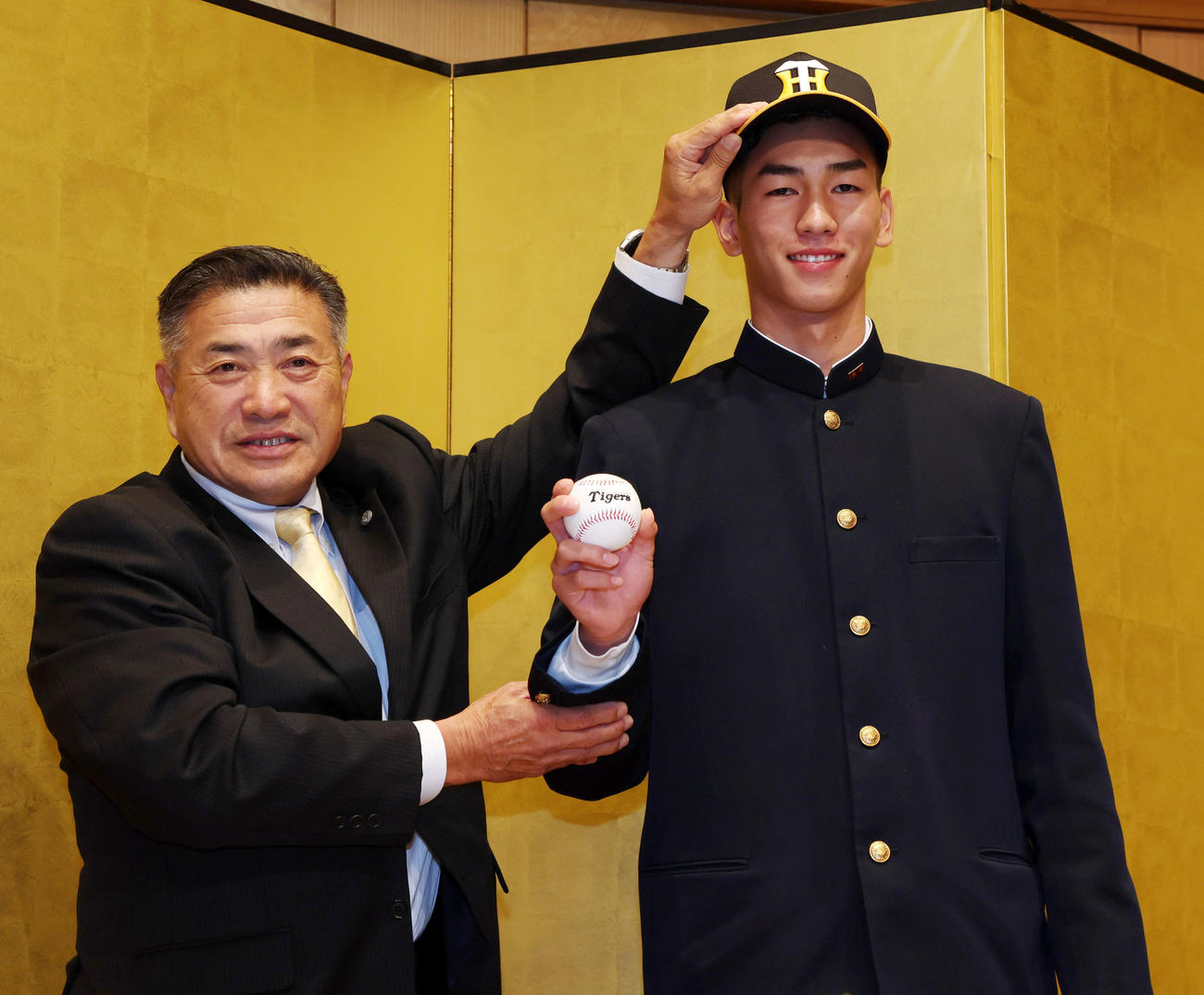 24年11月17日　仮契約を終え熊野スカウト（左）から帽子をかぶせてもらうドラフト2位指名の今朝丸（撮影・加藤哉）