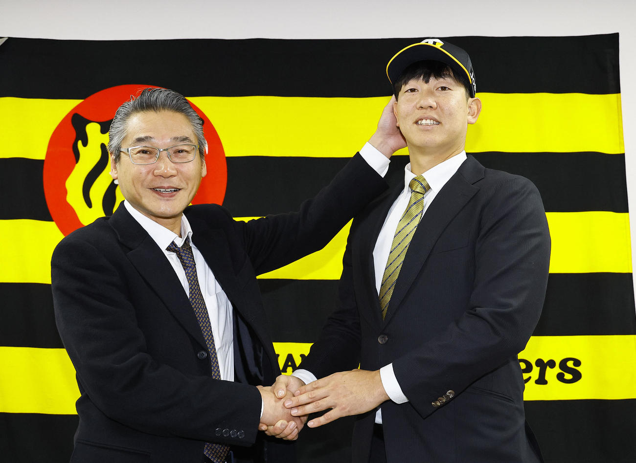入団会見を行い、嶌村球団本部長（左）に帽子をかぶせてもらう阪神畠（撮影・藤尾明華）