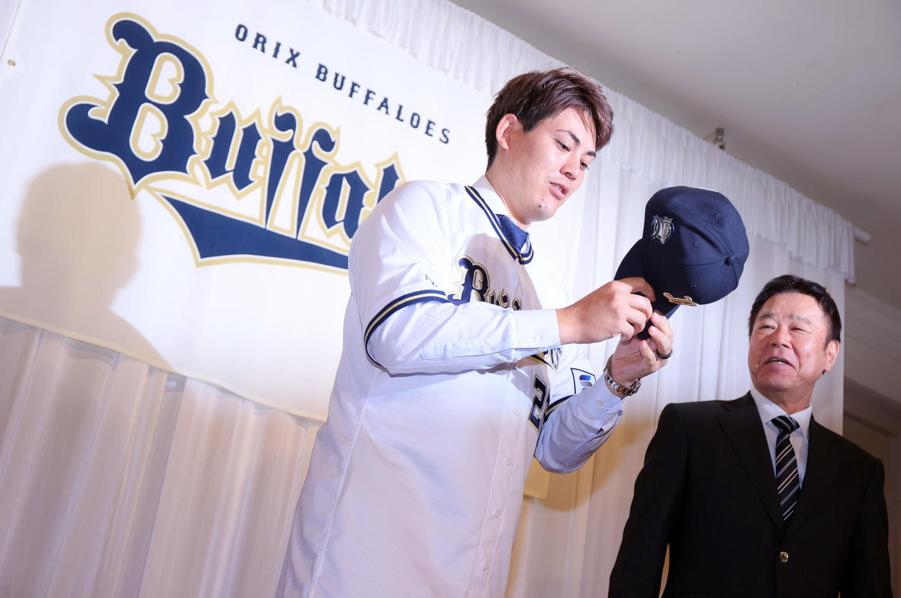 オリックス入団会見を終えた九里はユニホームに袖を通しフォトセッションに臨む。右はオリックス福良GM（撮影・上山淳一）