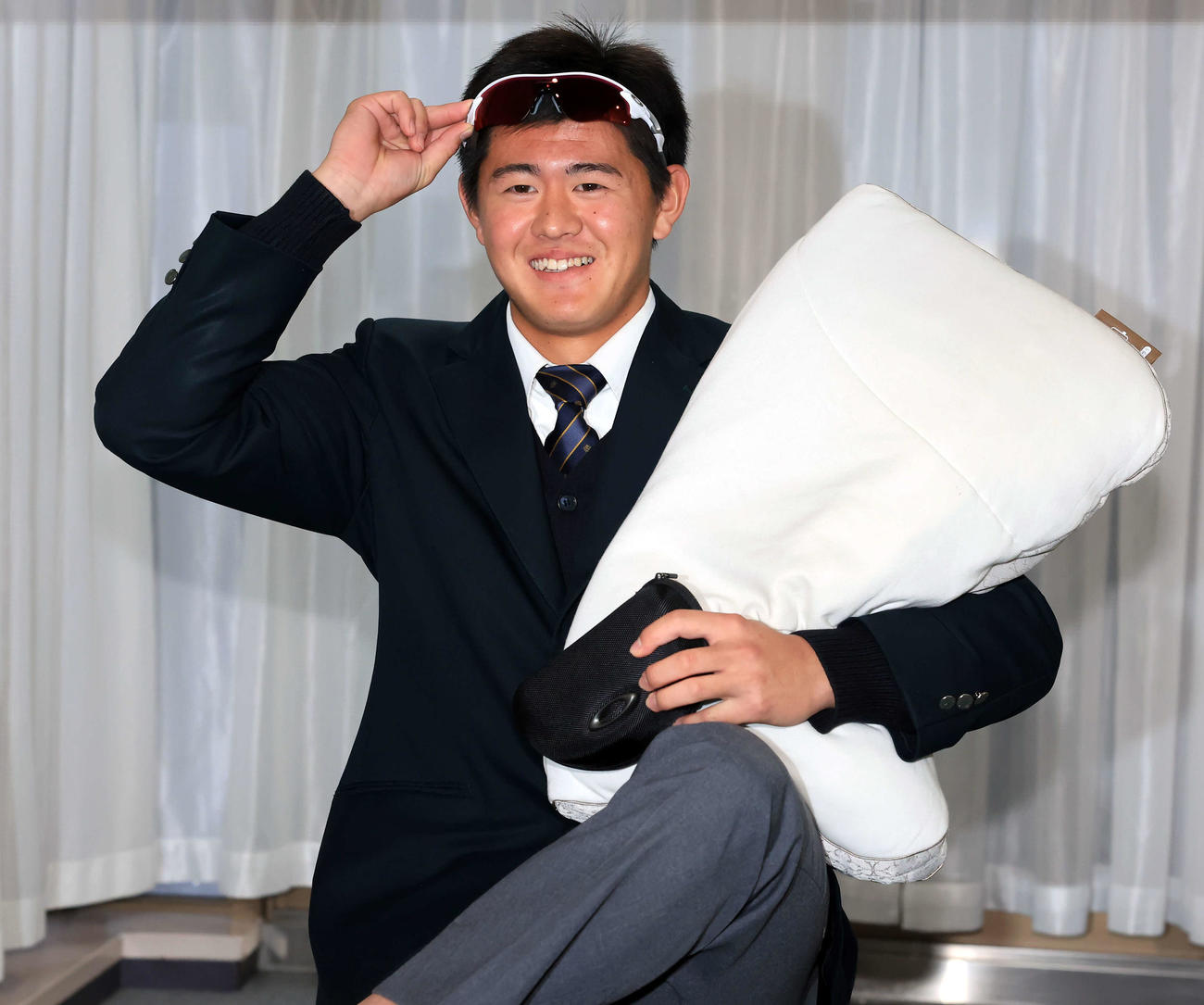 千葉ロッテマリーンズ寮に入寮した坂井は、持参した枕とサングラスを手に笑顔（撮影・浅見桂子）