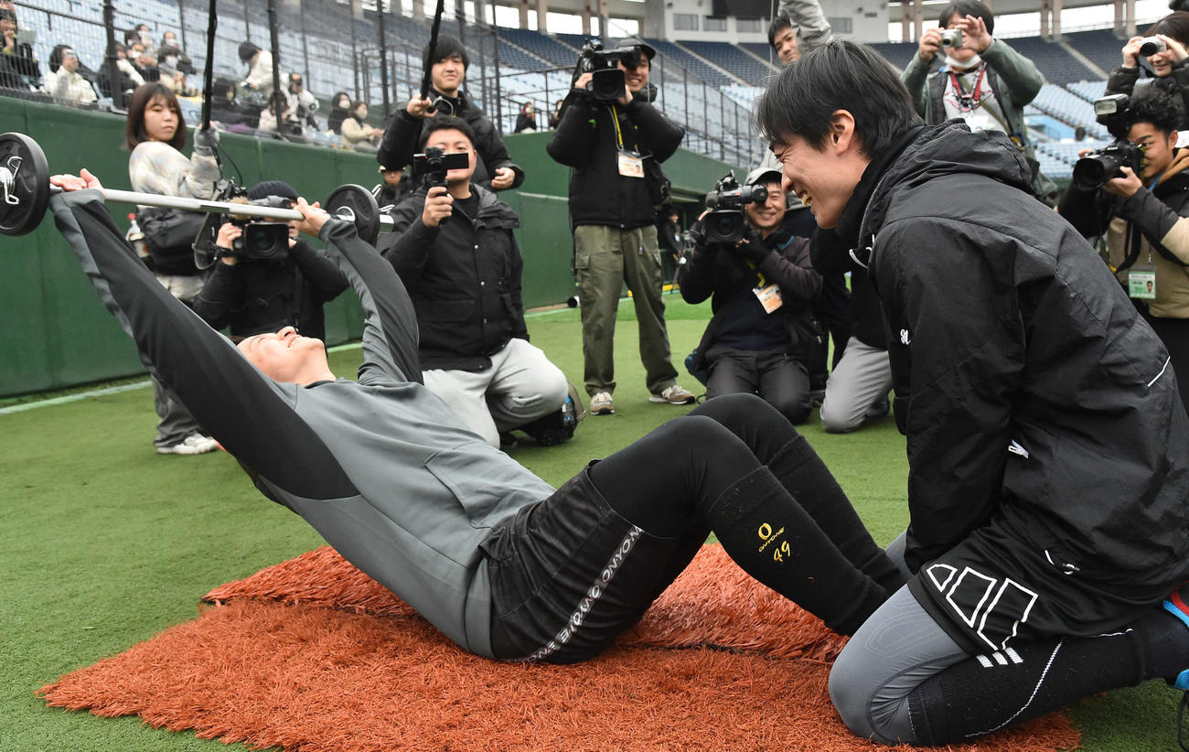 和田毅氏（右）に足を支えてもらい、バーベルを持って腹筋を行う阪神大竹（撮影・岩下翔太）