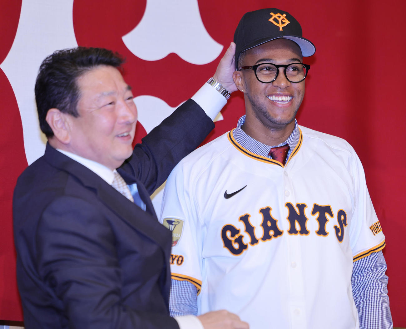 入団会見で吉村編成本部長（左）から帽子をかぶせられる巨人マルティネス（撮影・野上伸悟）