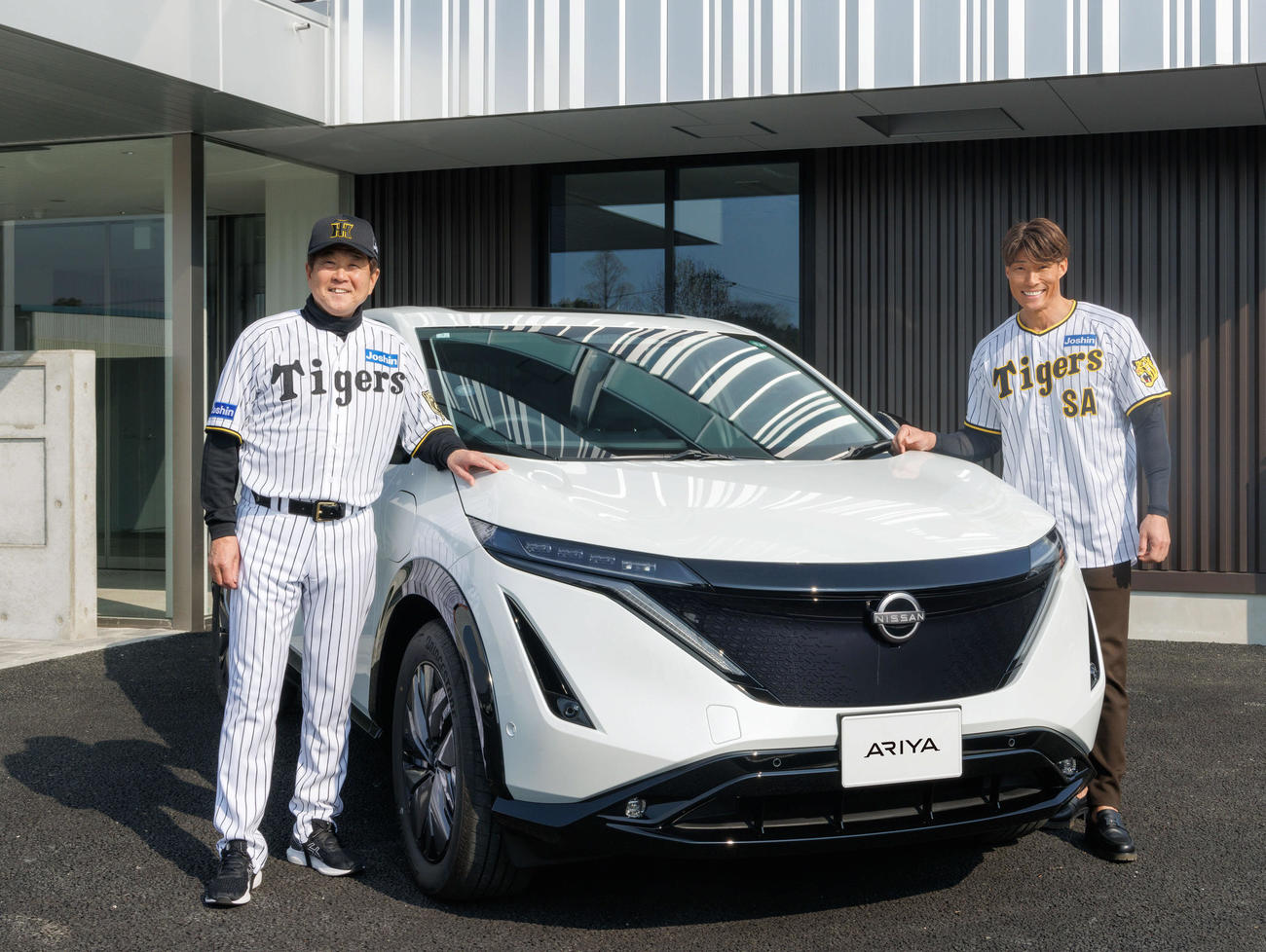 ゼロカーボンベースボールパークの社用車に導入した日産アリアの前で笑顔を見せる平田2軍監督（左）と糸井SA（球団提供）