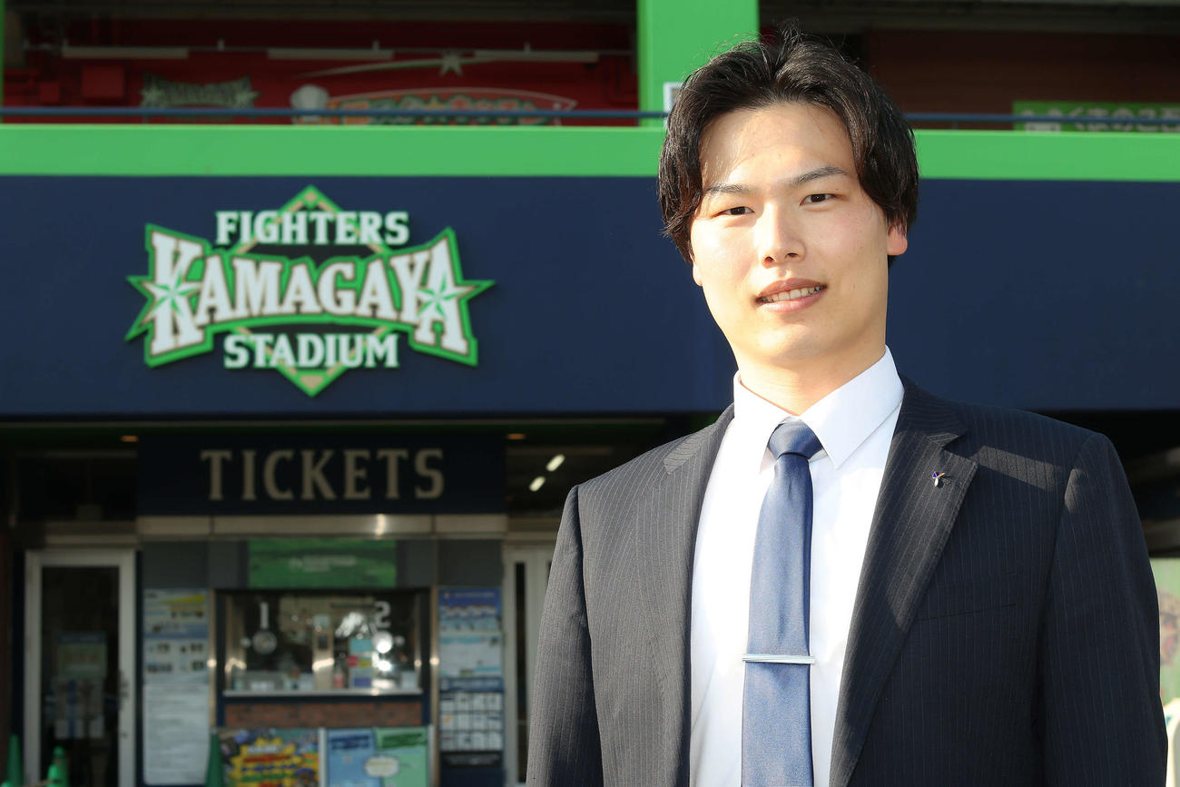 ファイターズ鎌ケ谷スタジアムを背に写真に納まる司法修習生の岩切さん（撮影・河田真司）