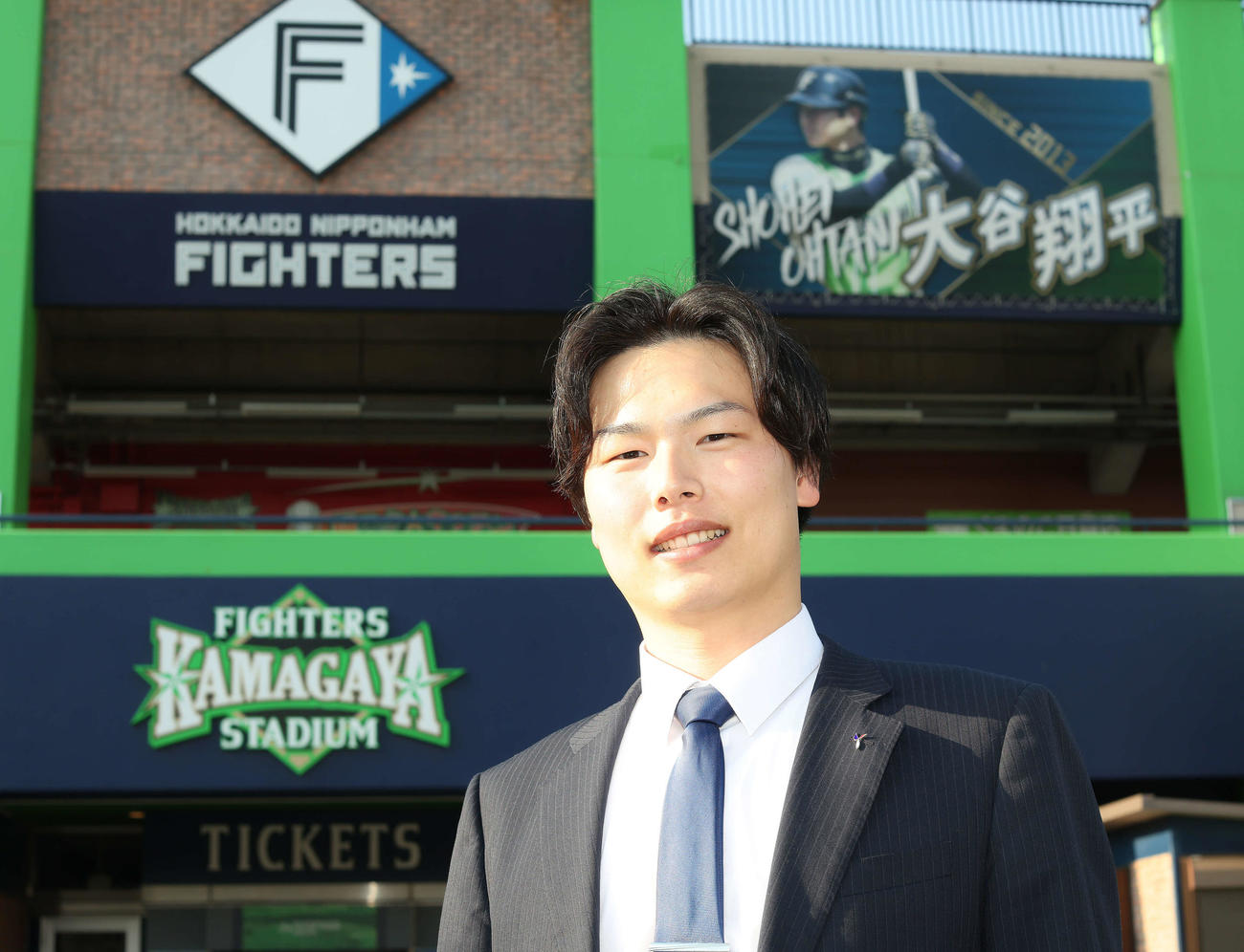ファイターズ鎌ケ谷スタジアムを背に写真に納まる司法修習生の岩切さん（撮影・河田真司）