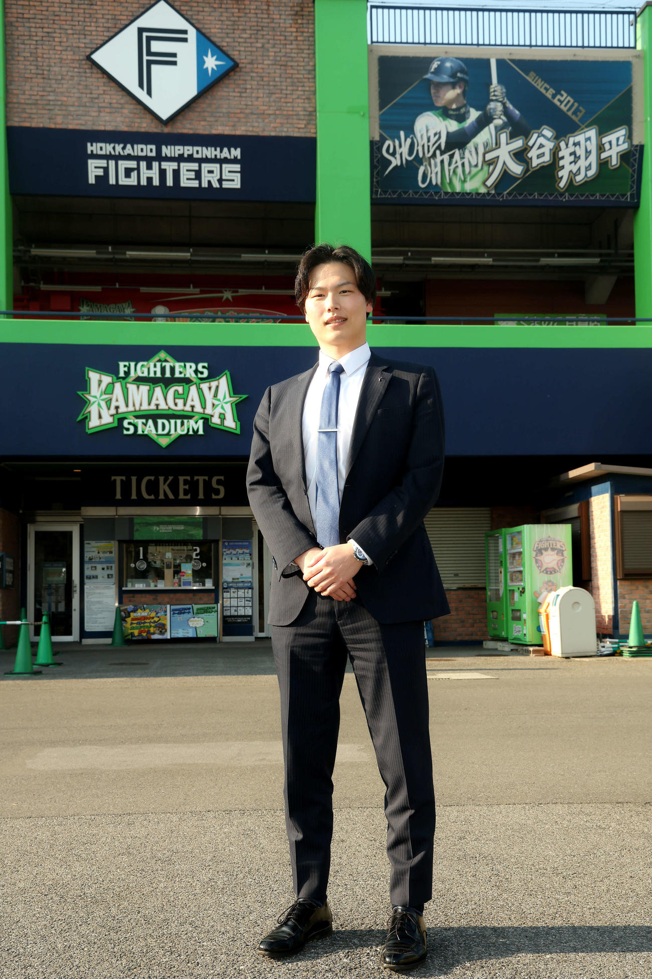 ファイターズ鎌ケ谷スタジアムを背に写真に納まる司法修習生の岩切さん（撮影・河田真司）