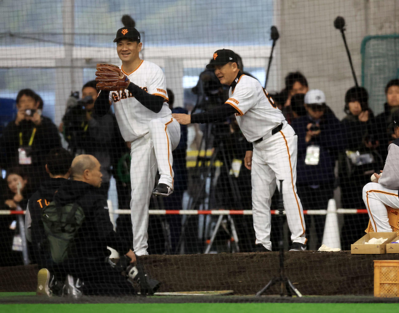 キャンプ初日、大勢の報道陣が見つめる中、逆傾斜のブルペンで巨人久保巡回投手コーチ（右）から投球フォームの指導を受けながら思わず笑顔の田中将（撮影・浅見桂子）