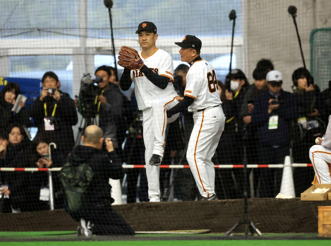 キャンプ初日、大勢の報道陣が見つめる中、ブルペンで巨人久保巡回投手コーチ（右）から投球フォームの指導を受ける田中将（撮影・浅見桂子）