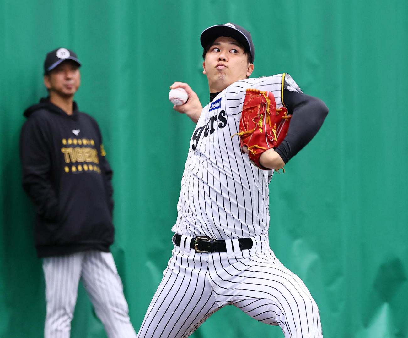 藤川監督（左）が見つめる中、ブルベンで投球練習をする才木（撮影・藤尾明華）