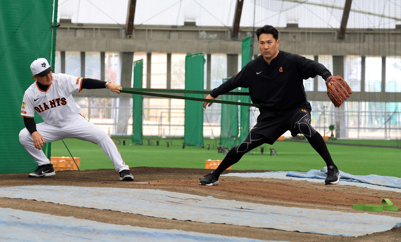 キャンプ3日目、ブルペンで巨人久保巡回投手コーチ（左）とチューブでトレーニングする田中将（撮影・浅見桂子）