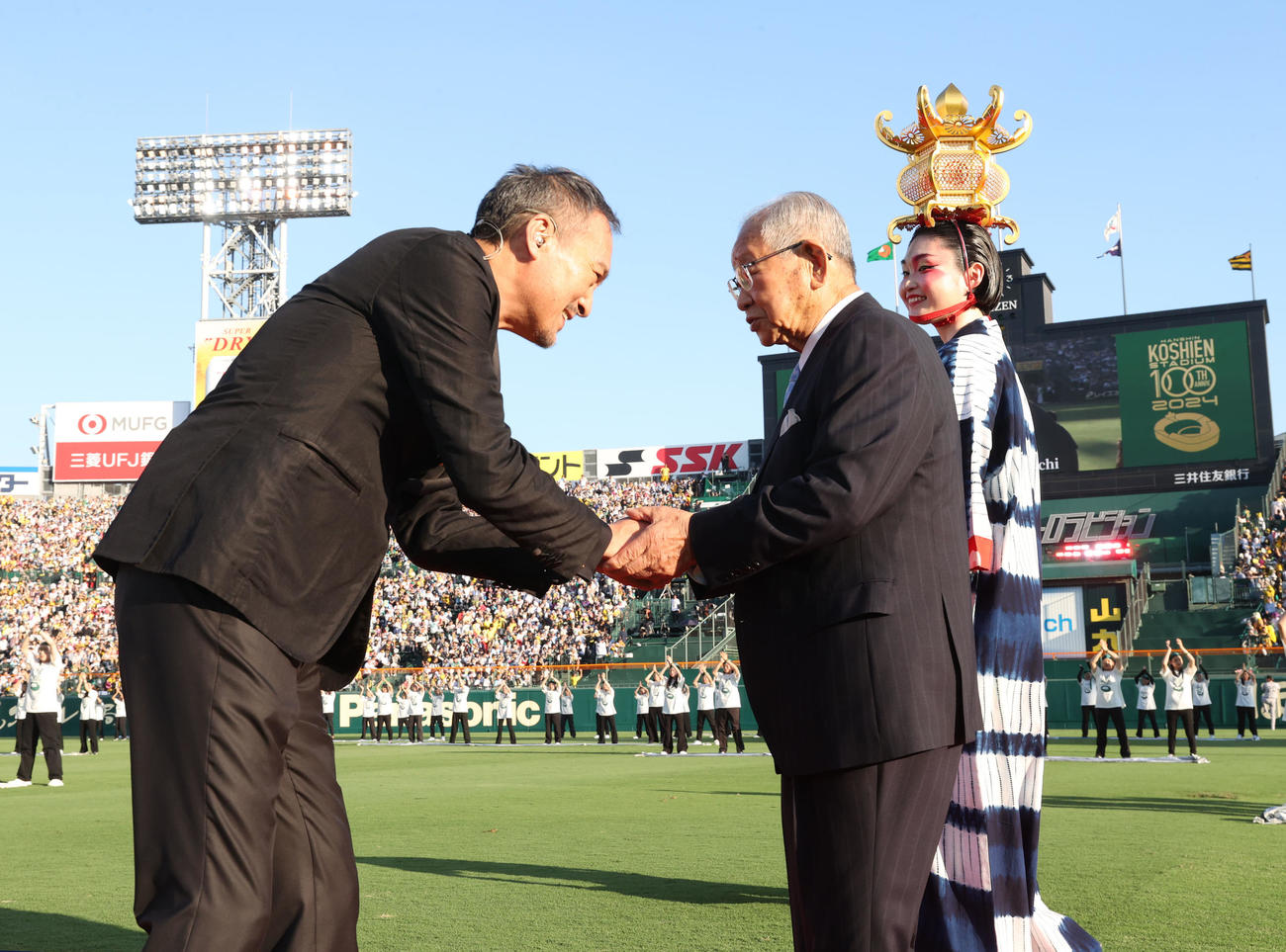 2024年8月1日、阪神対巨人　100周年セレモニーに出席し、俳優の渡辺謙さん（左）と握手を交わす阪神OBの吉田義男氏