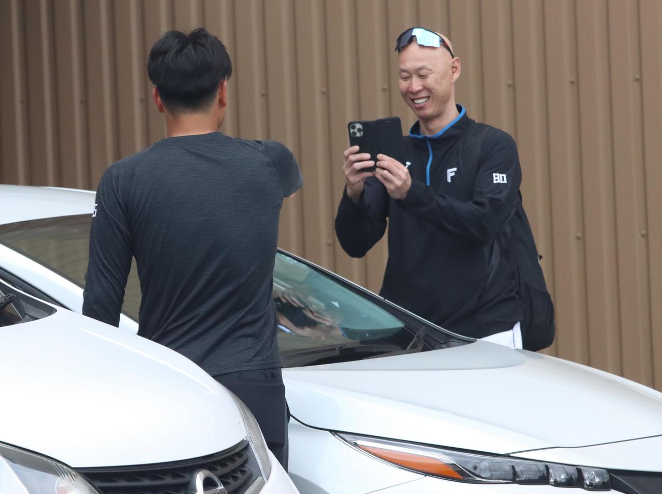 フロントガラスが割れた車の前で明瀬諒介（手前）の写真を撮影する森本稀哲外野守備走塁コーチ（2024年11月撮影）