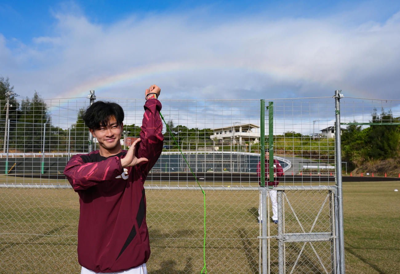 笑顔で体を動かす楽天古謝。後ろには大きな虹がかかった（撮影・鈴木みどり）