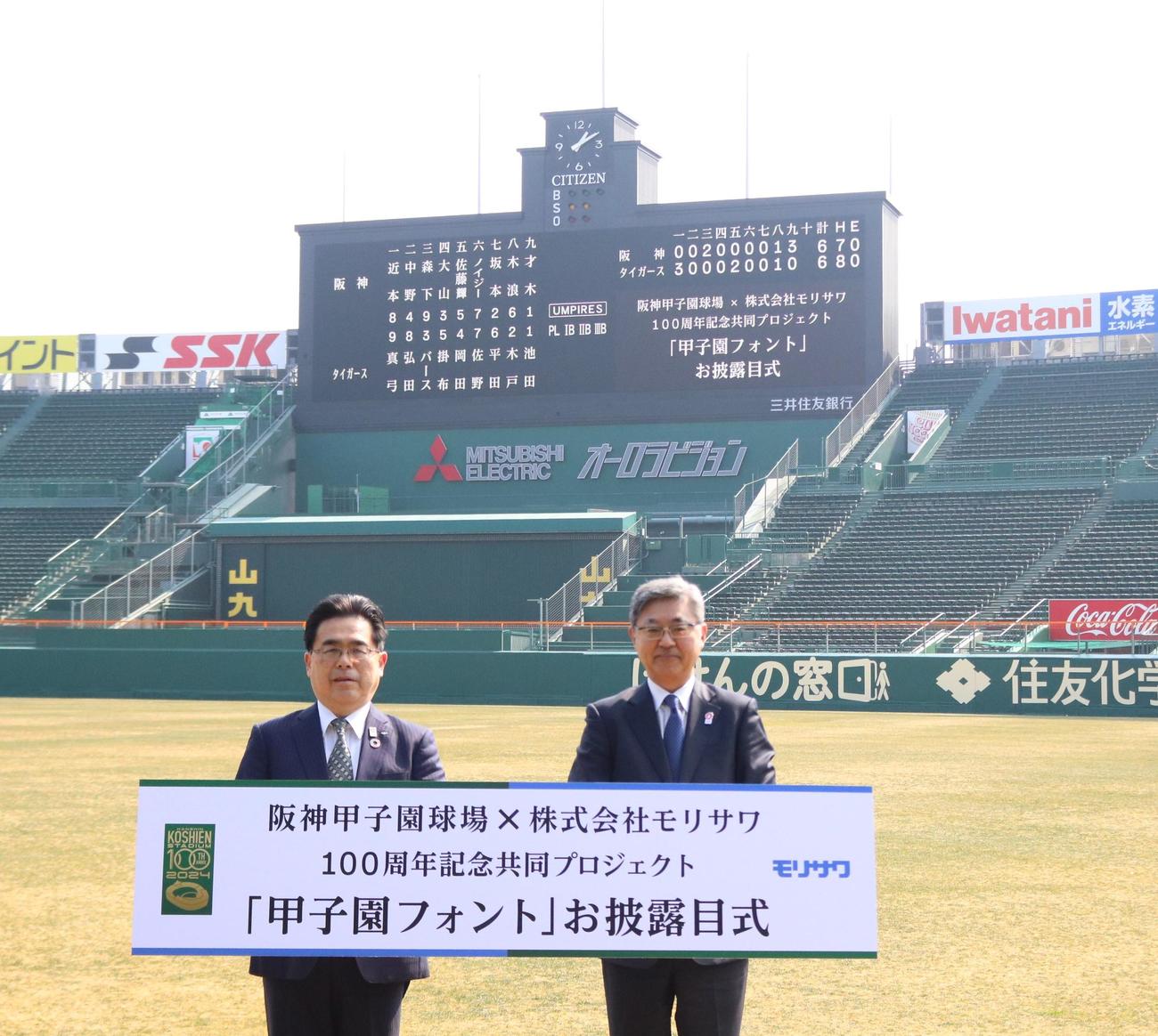 甲子園フォントで表示されたスコアボードを前に記念撮影する阪神電鉄谷本修取締役（左）と株式会社モリサワの森沢彰彦代表取締役社長（撮影・林亮佑）
