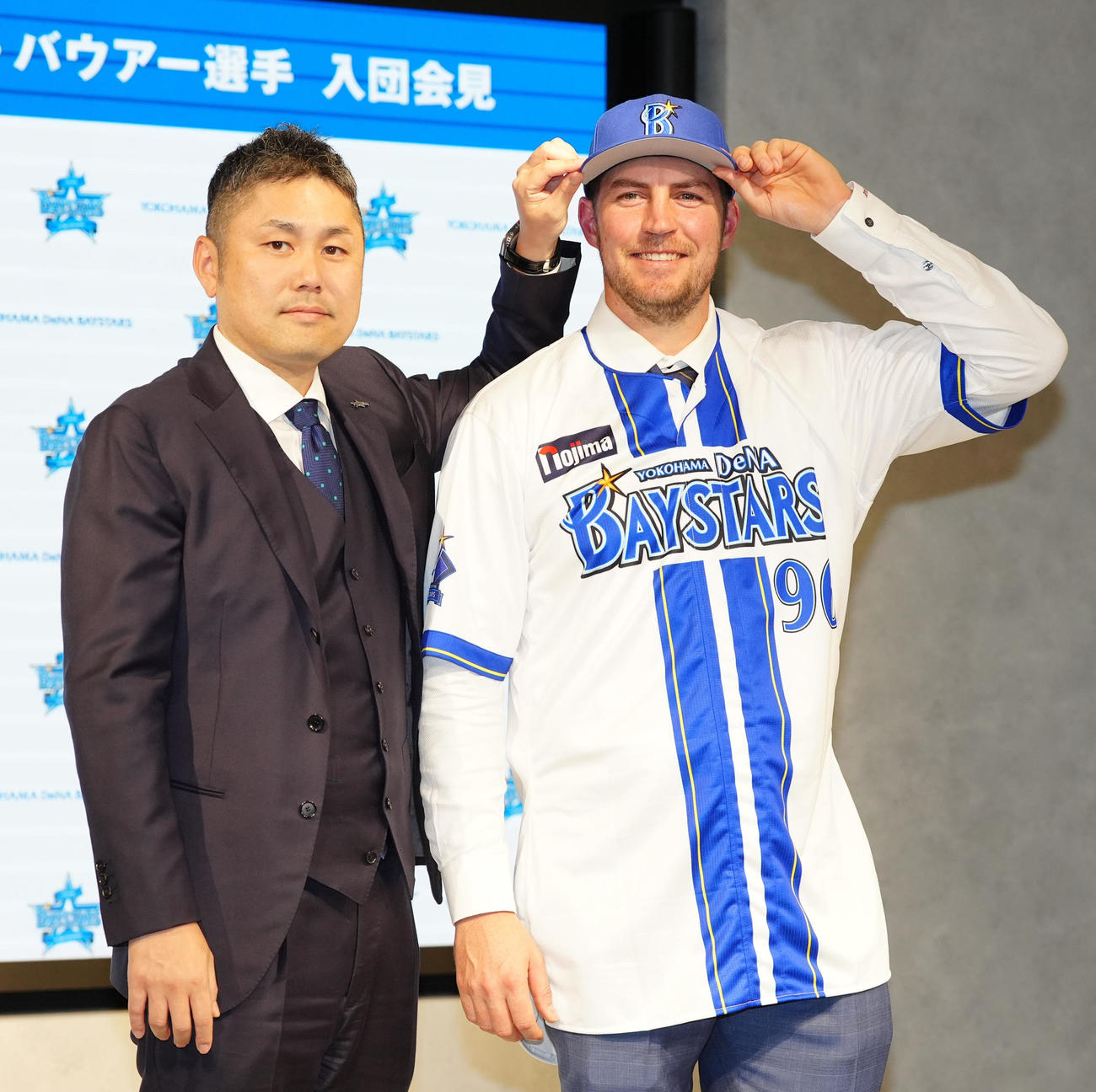 入団会見に臨み、DeNA萩原チーム統括本部長（左）と写真に納まるバウアー（撮影・江口和貴）