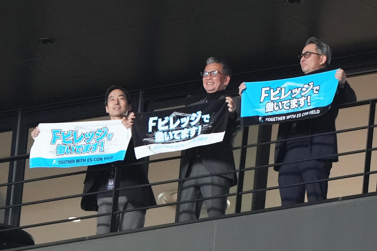 試合前、タオルを掲げる日本ハムの、左から三谷副本部長、小村社長、前沢本部長（撮影・足立雅史）