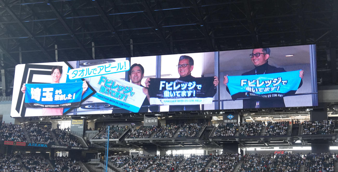 試合前、タオルを掲げる姿が大型映像に映し出される日本ハムの、左から三谷副本部長、小村社長、前沢本部長（撮影・足立雅史）