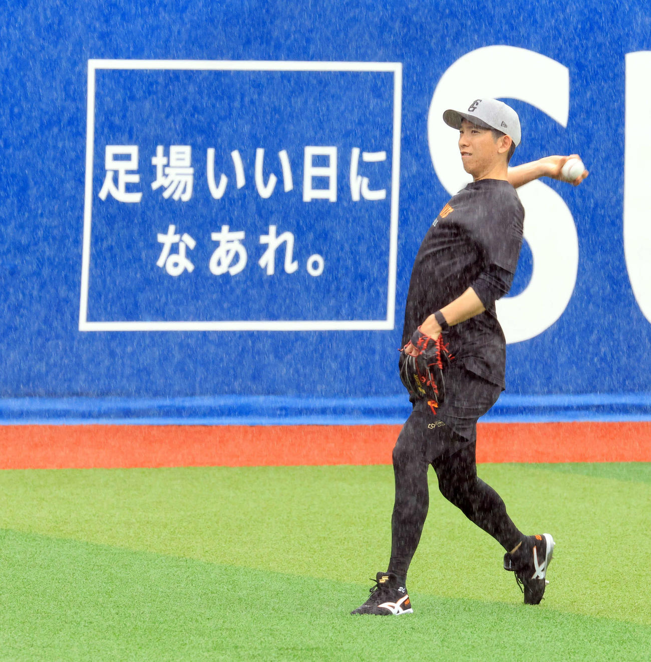 DeNA対巨人　雨天の中、「足場いい日になあれ・」の看板を背にキャッチボールする巨人戸郷（撮影・浅見桂子）