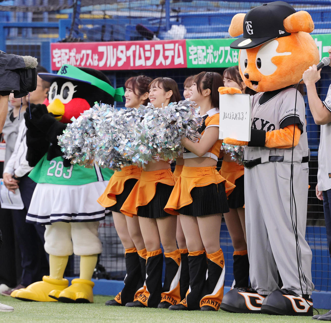 ヤクルト対巨人　試合前に登場したジャビッ（右端）は、つば九郎が愛した言葉「みんなえみふる！」と記したフリップを出す。左端はつばみ（撮影・野上伸悟）