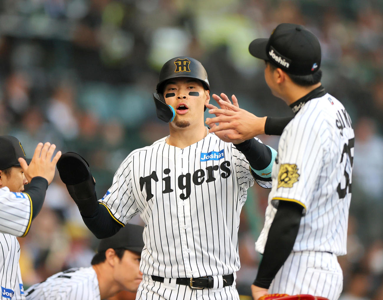 二走佐藤輝明（左）は前川右京の一ゴロの悪送球で生還し才木浩人から出迎えを受ける