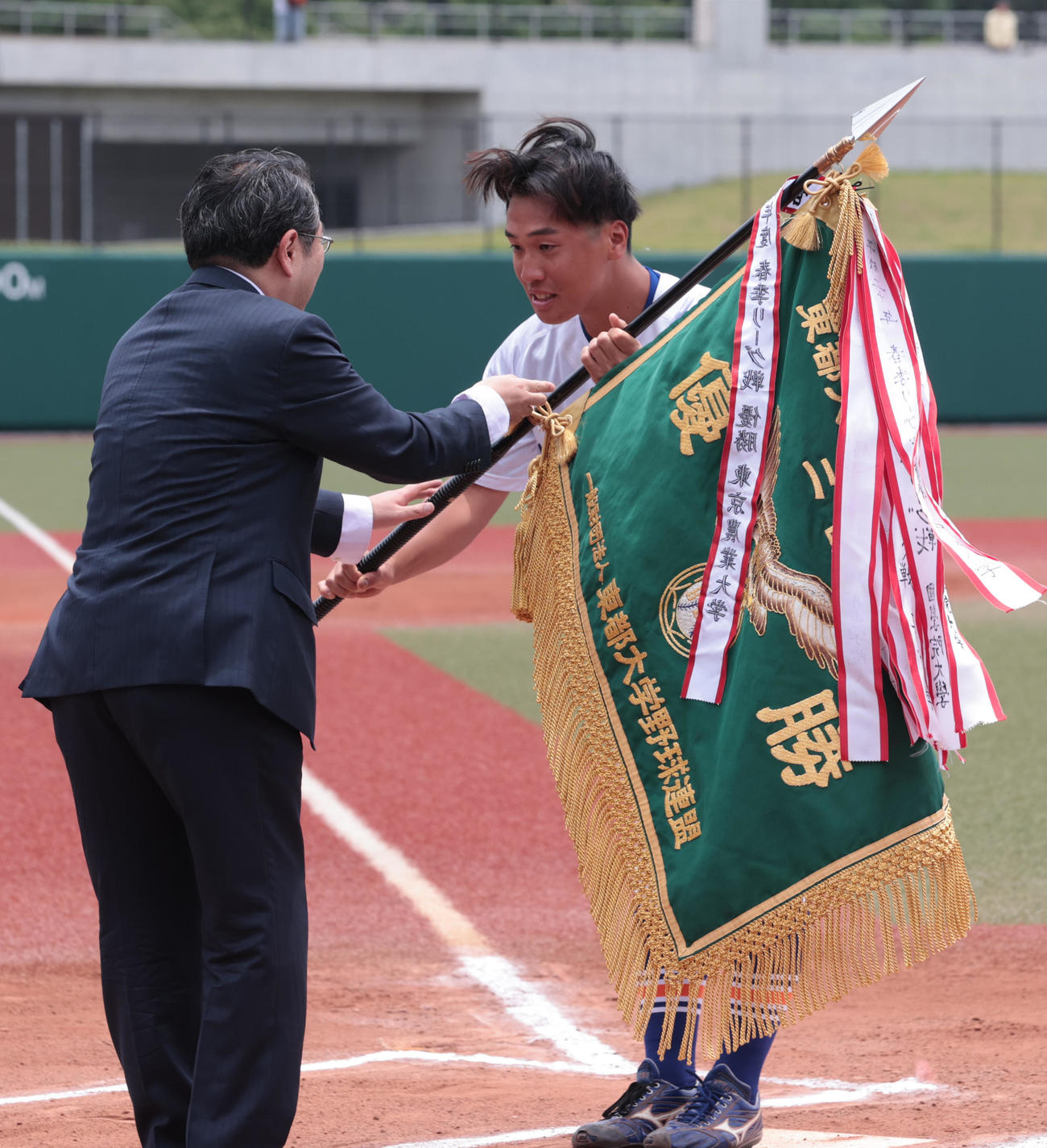 東都大学2部優勝決定戦を制した駒大・出村主将（右）は優勝旗を受け取る＝2025年6月6日（撮影・柴田隆二）