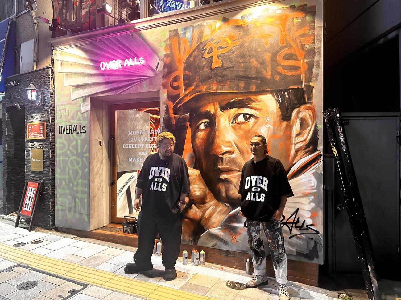 外苑駅前の「OVER ALLs」のオフィスの外壁に故長嶋茂雄さんの壁画を描いた赤沢さん（左）と山本さん（撮影・平山連）