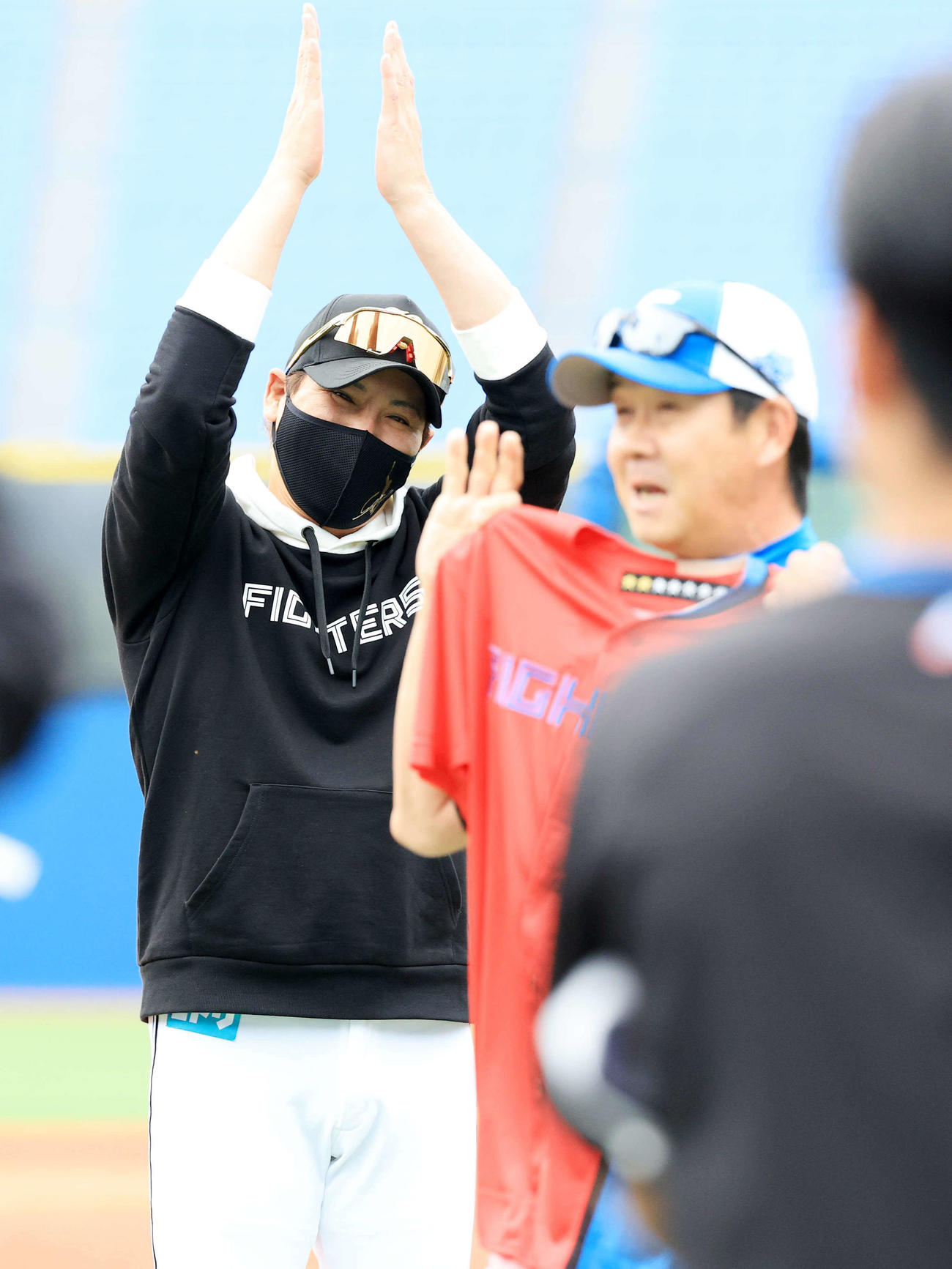 DeNA対日本ハム　試合前、この日60歳を迎えた日本ハム八木打撃コーチ（手前）をお祝いして赤いユニホームを贈り、拍手する新庄監督（撮影・浅見桂子）