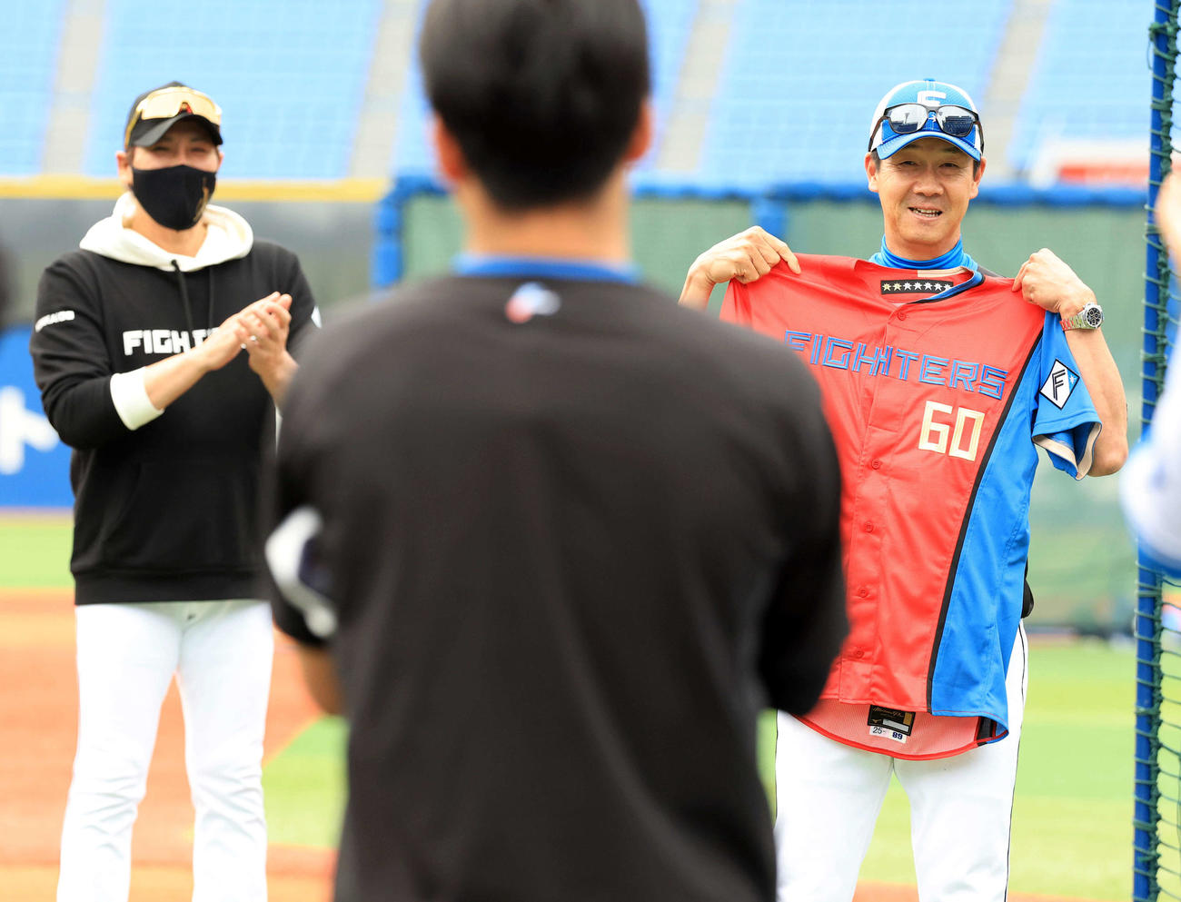 DeNA対日本ハム　試合前、この日60歳を迎えた日本ハム八木打撃コーチ（右）は赤いユニホームを贈られ笑顔。左は新庄監督（撮影・浅見桂子）