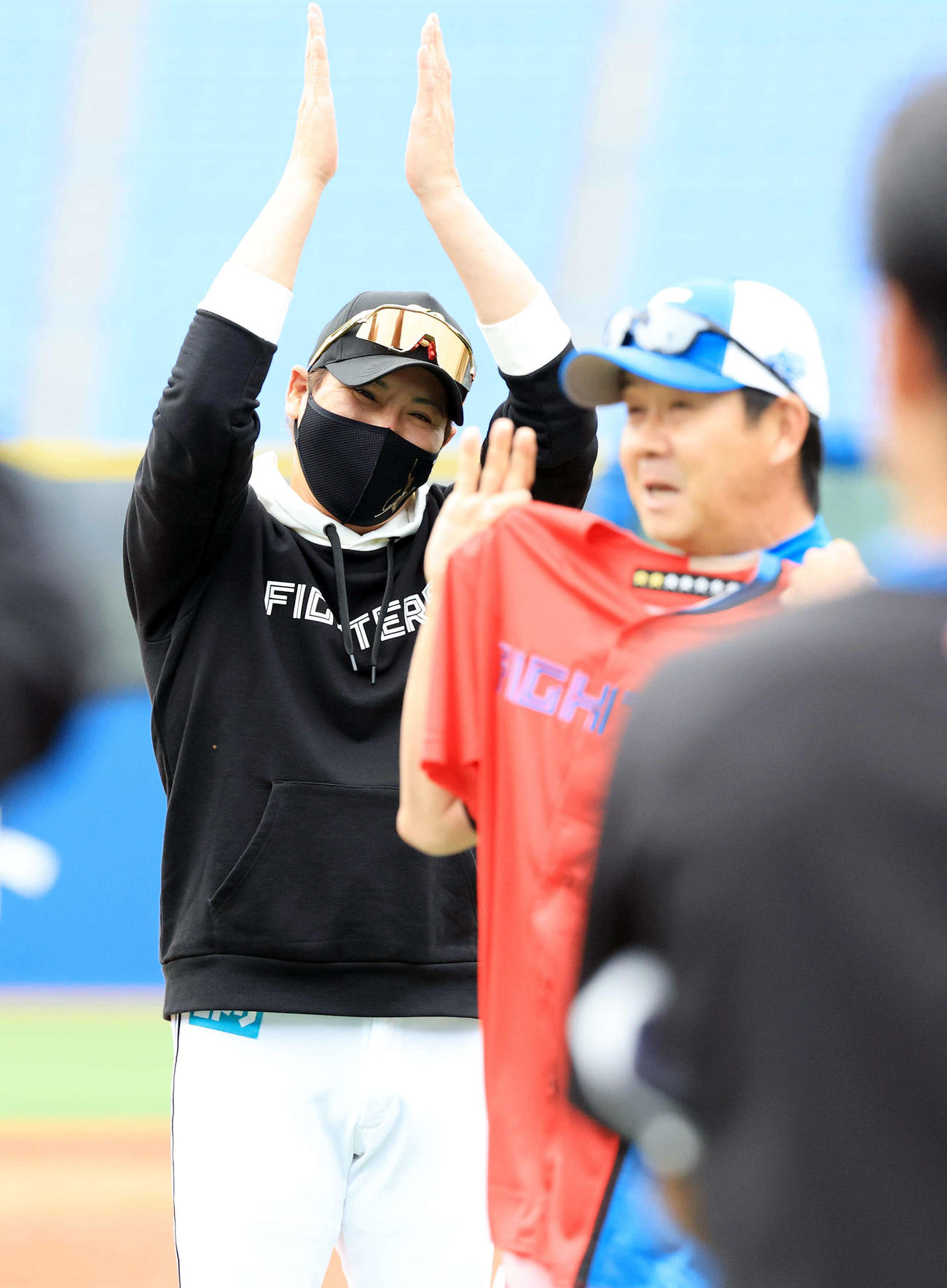 DeNA対日本ハム　試合前、この日60歳を迎えた日本ハム八木打撃コーチ（手前）をお祝いして赤いユニホームを贈り、拍手する新庄監督（撮影・浅見桂子）