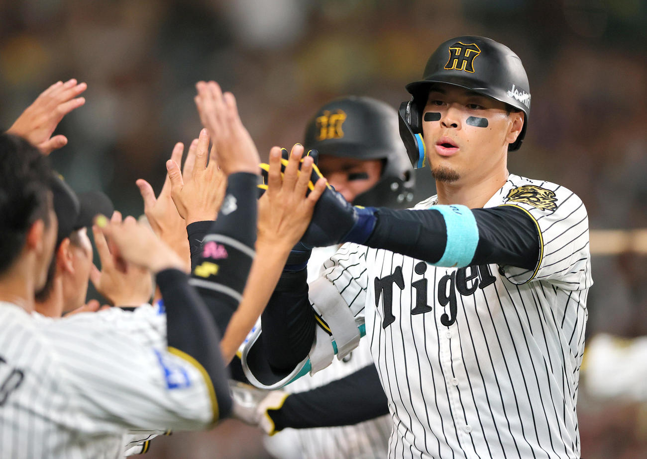 阪神対ロッテ　8回裏阪神2死二塁、佐藤輝は（右）は中越え2点本塁打を放ちナインの祝福を受ける（撮影・上山淳一）