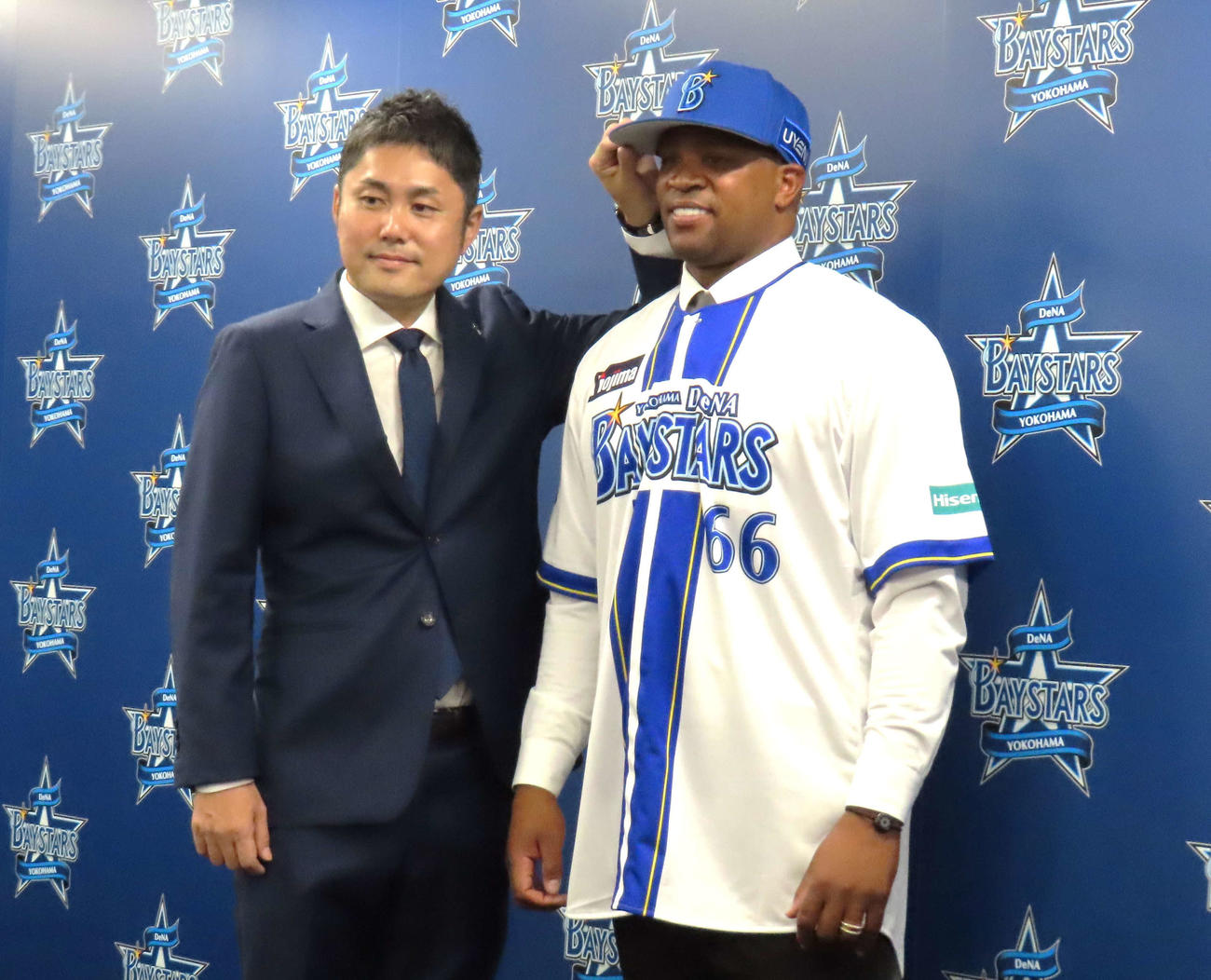 横浜市内の球団事務所で入団会見に登壇し、萩原チーム統括本部長（左）から帽子を被せてもらうDeNAビシエド
