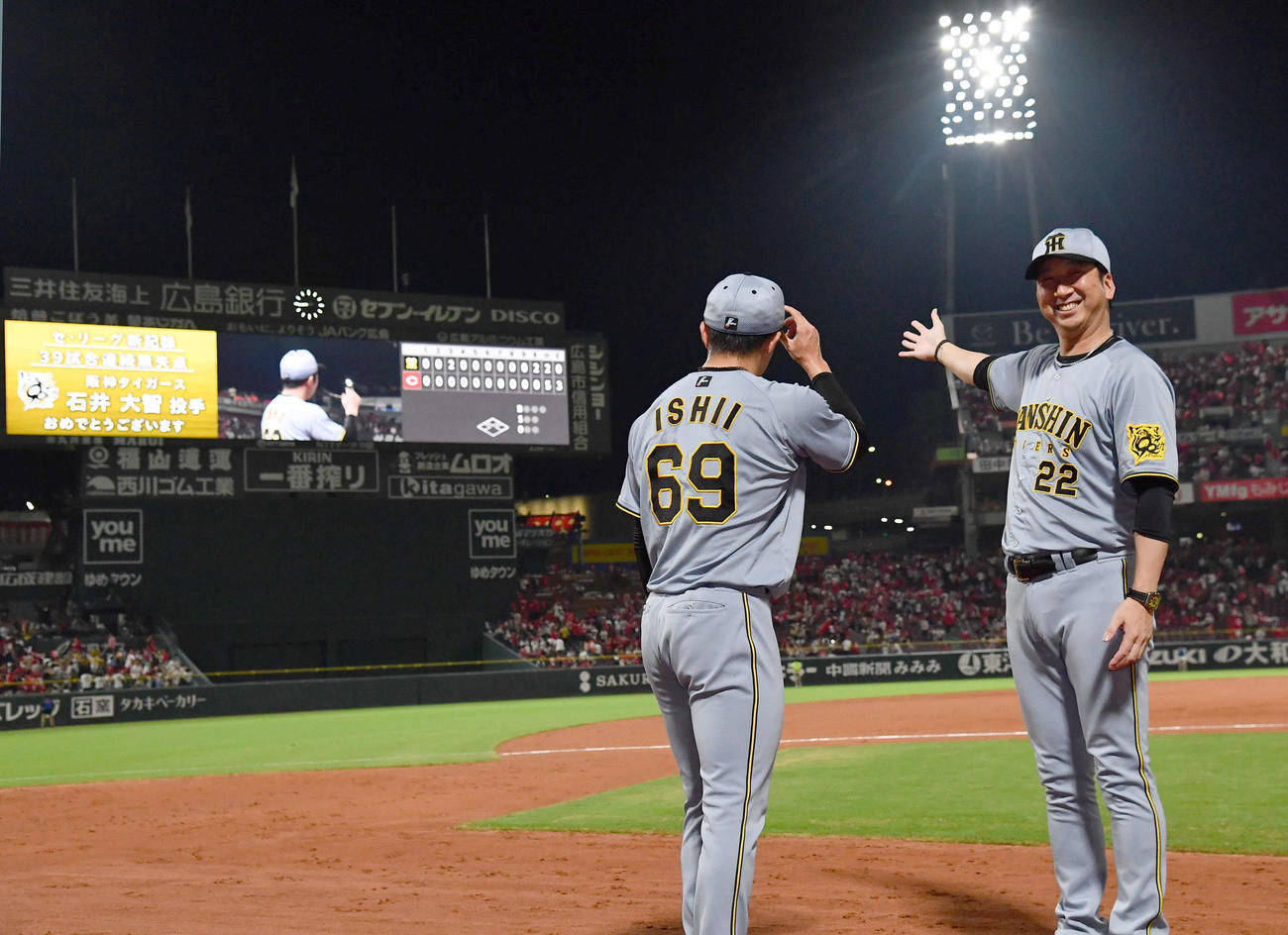 広島対阪神　セリーグ新記録となる39試合連続無失点を達成した石井（左）を祝福するバックスクリーンのメッセージを笑顔で示す藤川監督（撮影・岩下翔太）