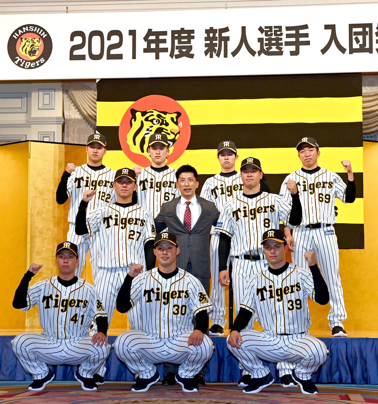 新人選手入団発表会でガッツポーズする下段右から栄枝裕貴、佐藤蓮、村上頌樹、中段右から佐藤輝明、矢野燿大監督、伊藤将司、上段右から石井大智、中野拓夢、高寺望夢、岩田将貴（2020年12月撮影）