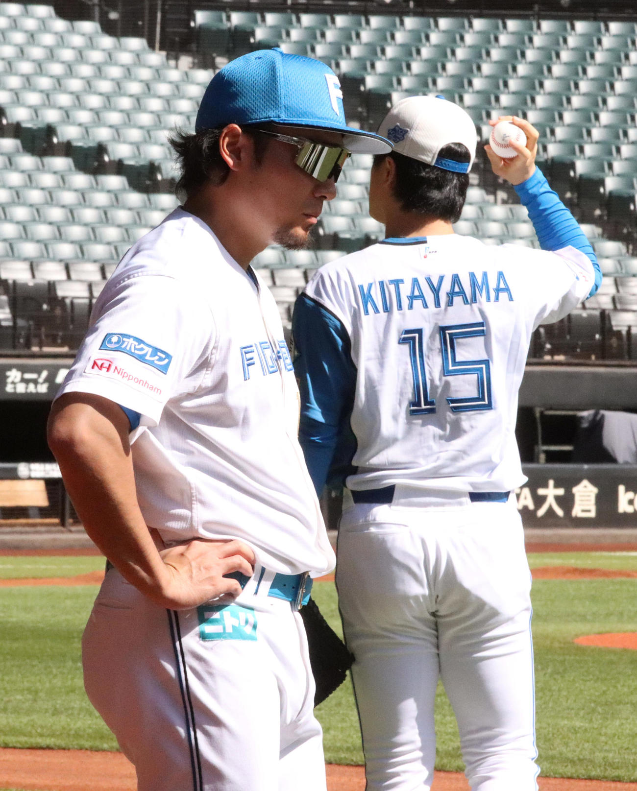 屋根が開き日差しの強いエスコンフィールドでサングラスをつけ調整する日本ハム伊藤（左）。右は北山
