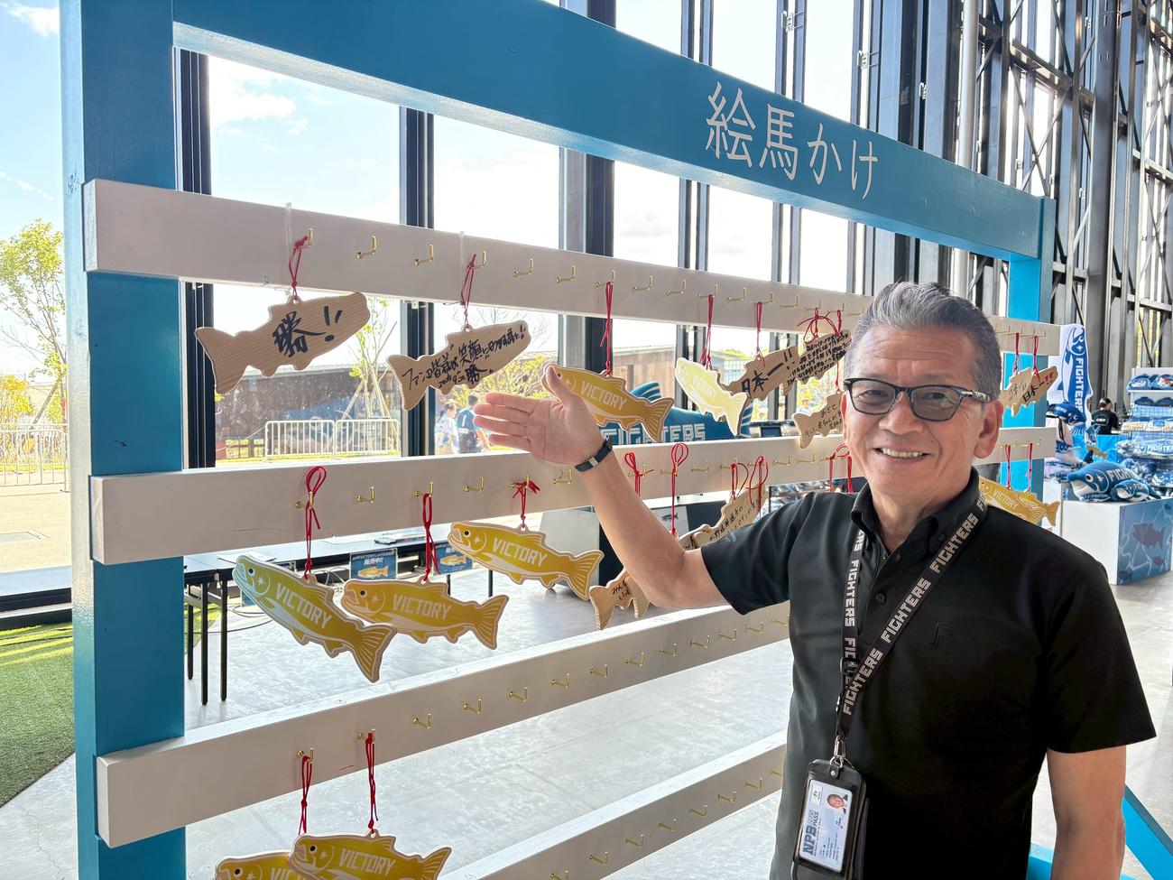 エスコンフィールド1階ガラスウォール前に設置されている「絵馬かけ」を紹介する日本ハム小村球団社長。自身も絵馬に「勝」の文字を書き優勝祈願