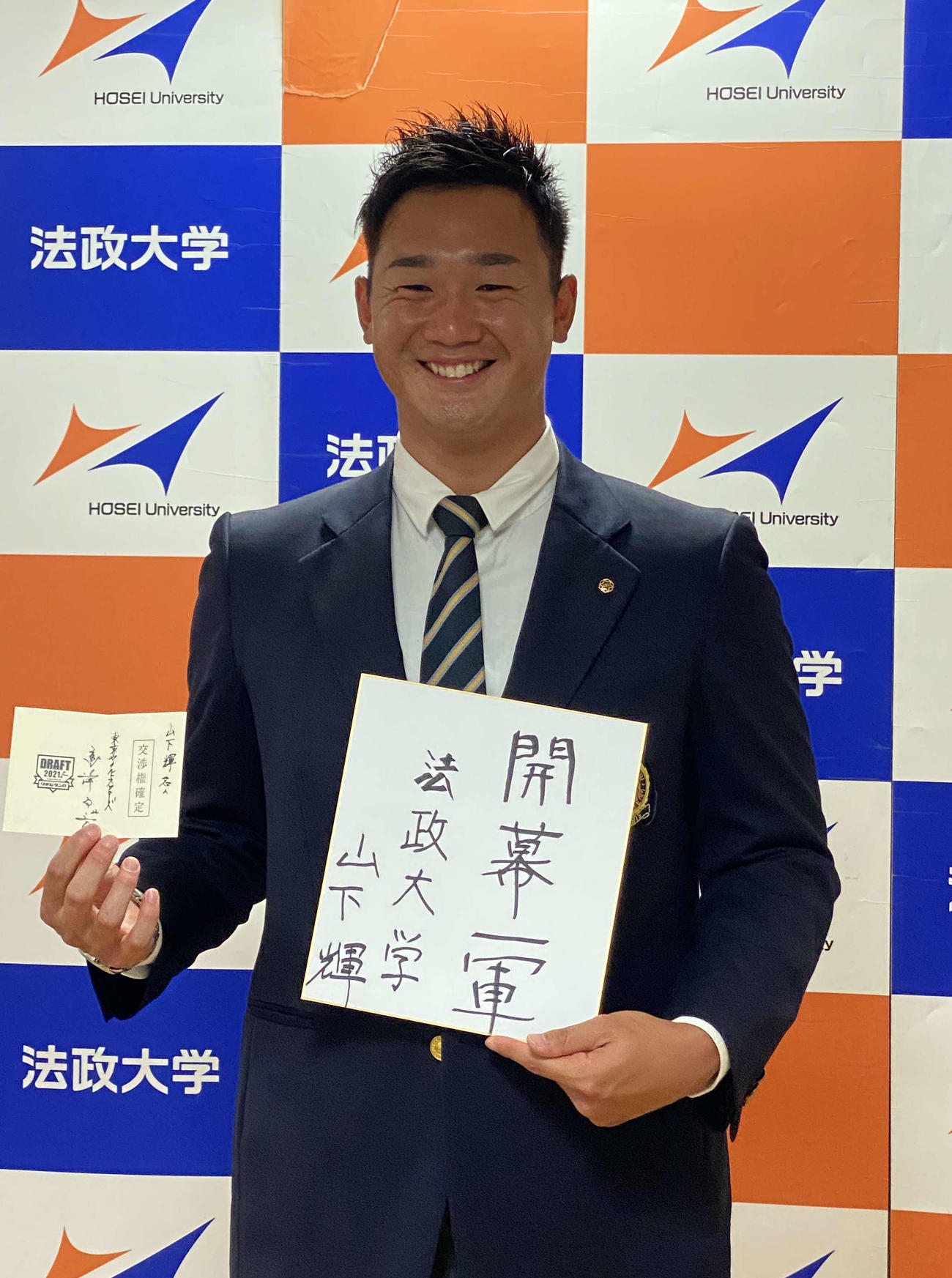 ヤクルトからドラフト1位の指名あいさつを受け、高津監督のメッセージ入り当たりくじと、抱負を書いた色紙を手にする法大・山下輝投手（2021年10月15日撮影）