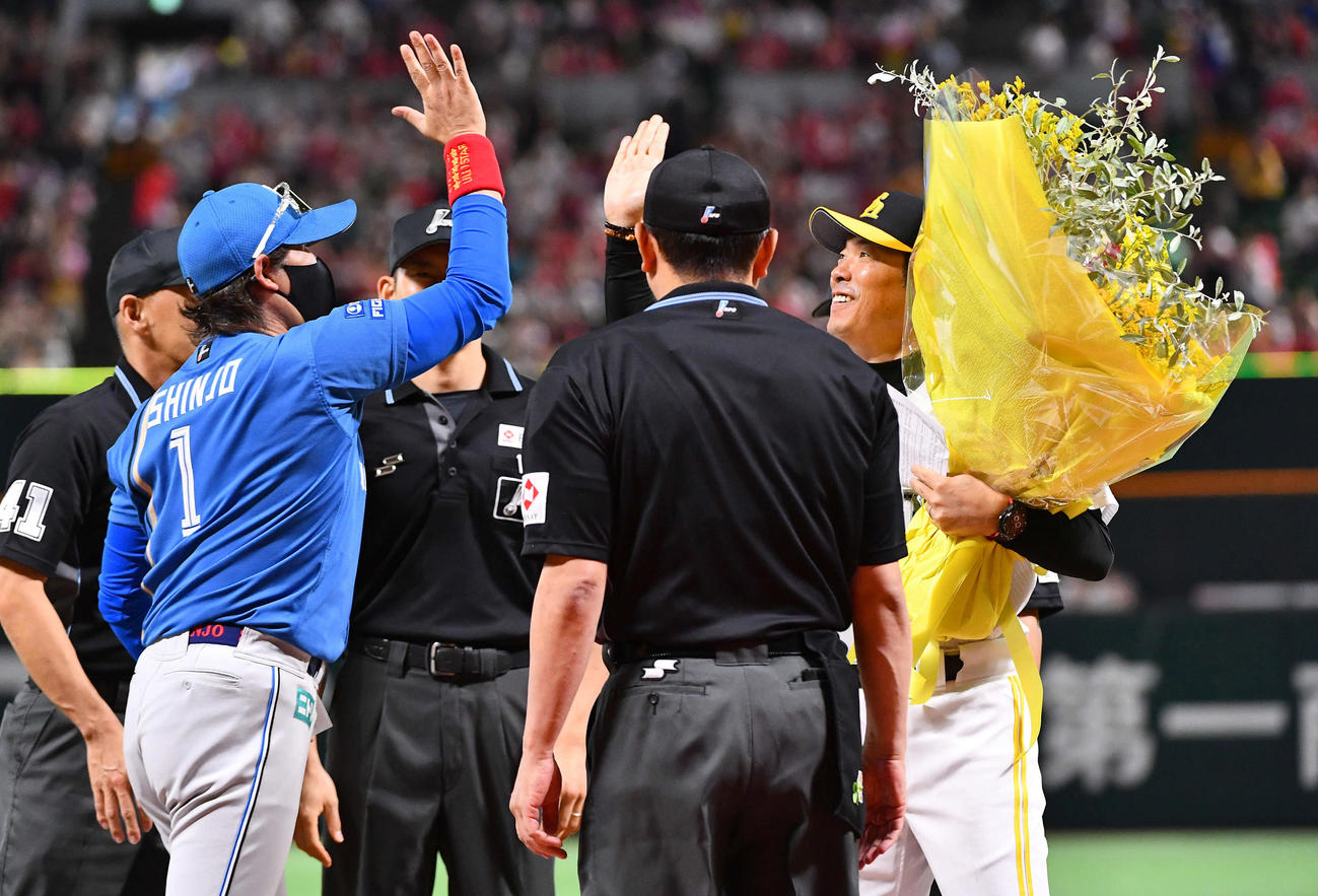 ソフトバンク対日本ハム　試合前のメンバー表交換で日本ハム新庄監督（左）からリーグ優勝のお祝いに黄色の花束を贈られ、笑顔でハイタッチするソフトバンク小久保監督（撮影・岩下翔太）