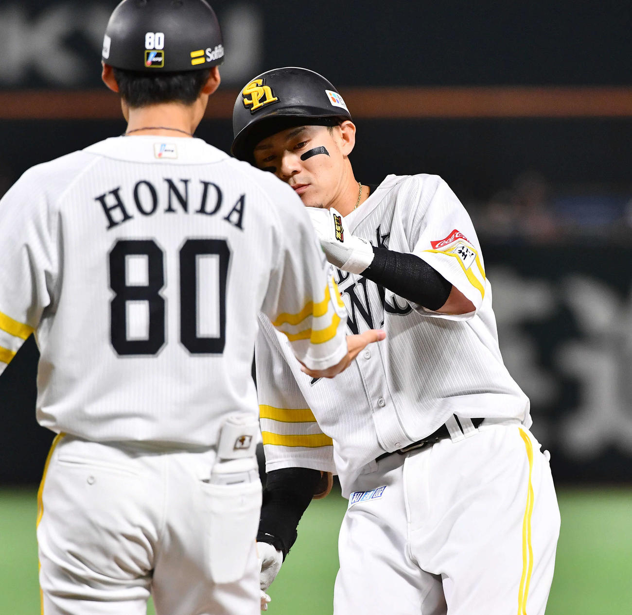 ソフトバンク対オリックス　1回裏ソフトバンク無死、左前安打で出塁した牧原大（右）は本多コーチとタッチを交わす（撮影・岩下翔太）
