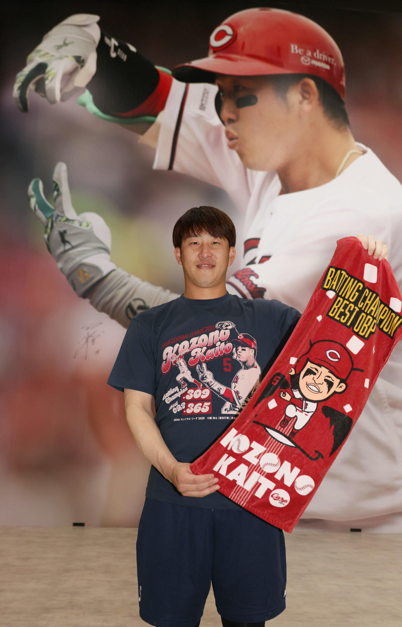 マツダスタジアム正面グッズ売り場の巨大壁面写真がリニューアル。タイトル記念グッズのTシャツを着てポーズを決める小園（撮影・加藤孝規）