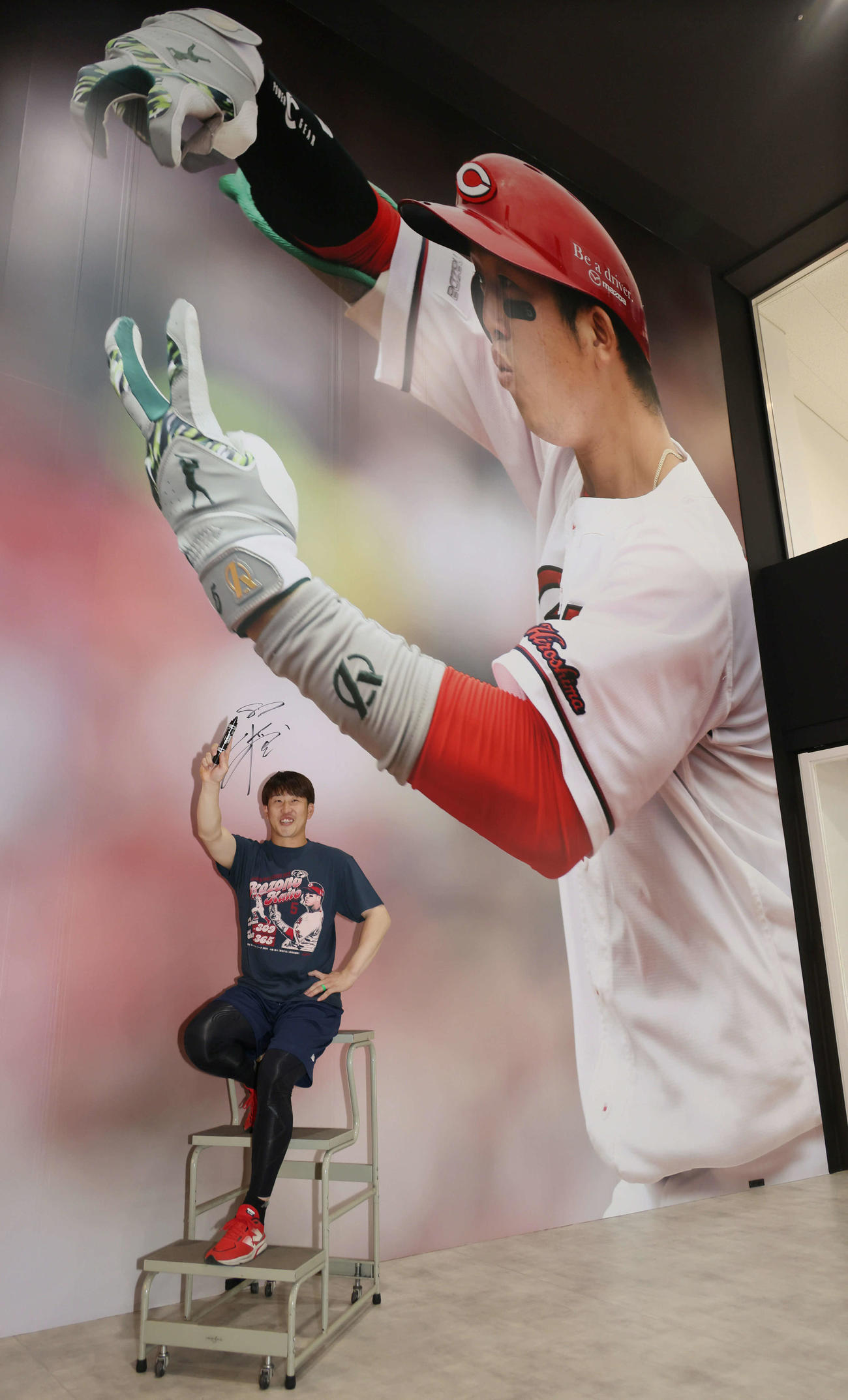 マツダスタジアム正面グッズ売り場の巨大壁面写真がリニューアル。タイトル記念グッズのTシャツを着てポーズを決める小園（撮影・加藤孝規）