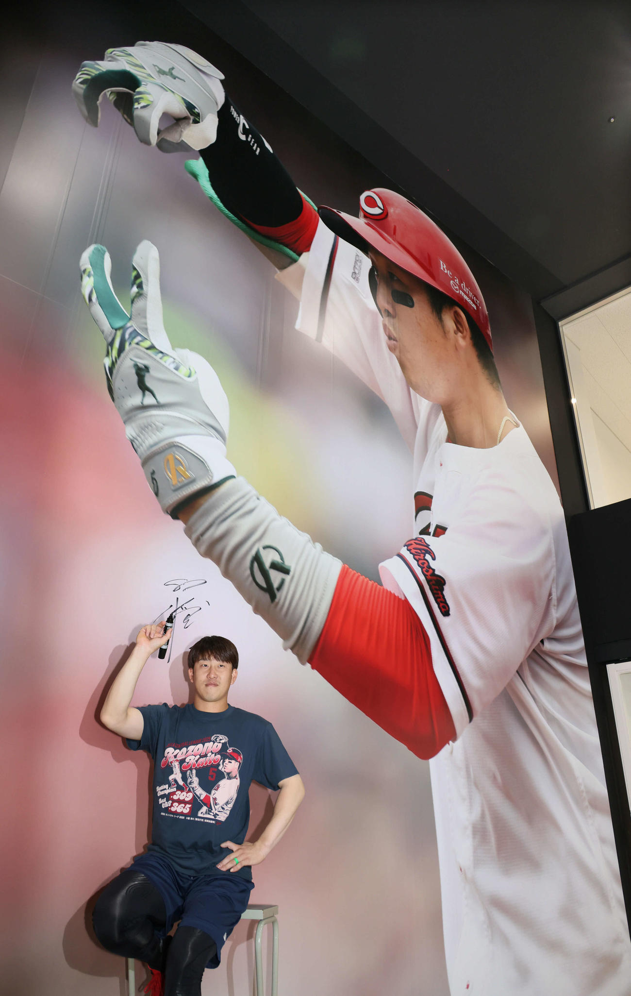 マツダスタジアム正面グッズ売り場の巨大壁面写真がリニューアル。タイトル記念グッズのTシャツを着てポーズを決める小園（撮影・加藤孝規）