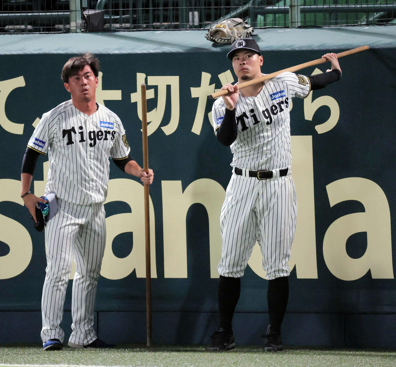 棒を使ってストレッチする阪神佐藤輝。左は桐敷（撮影・宮崎幸一）