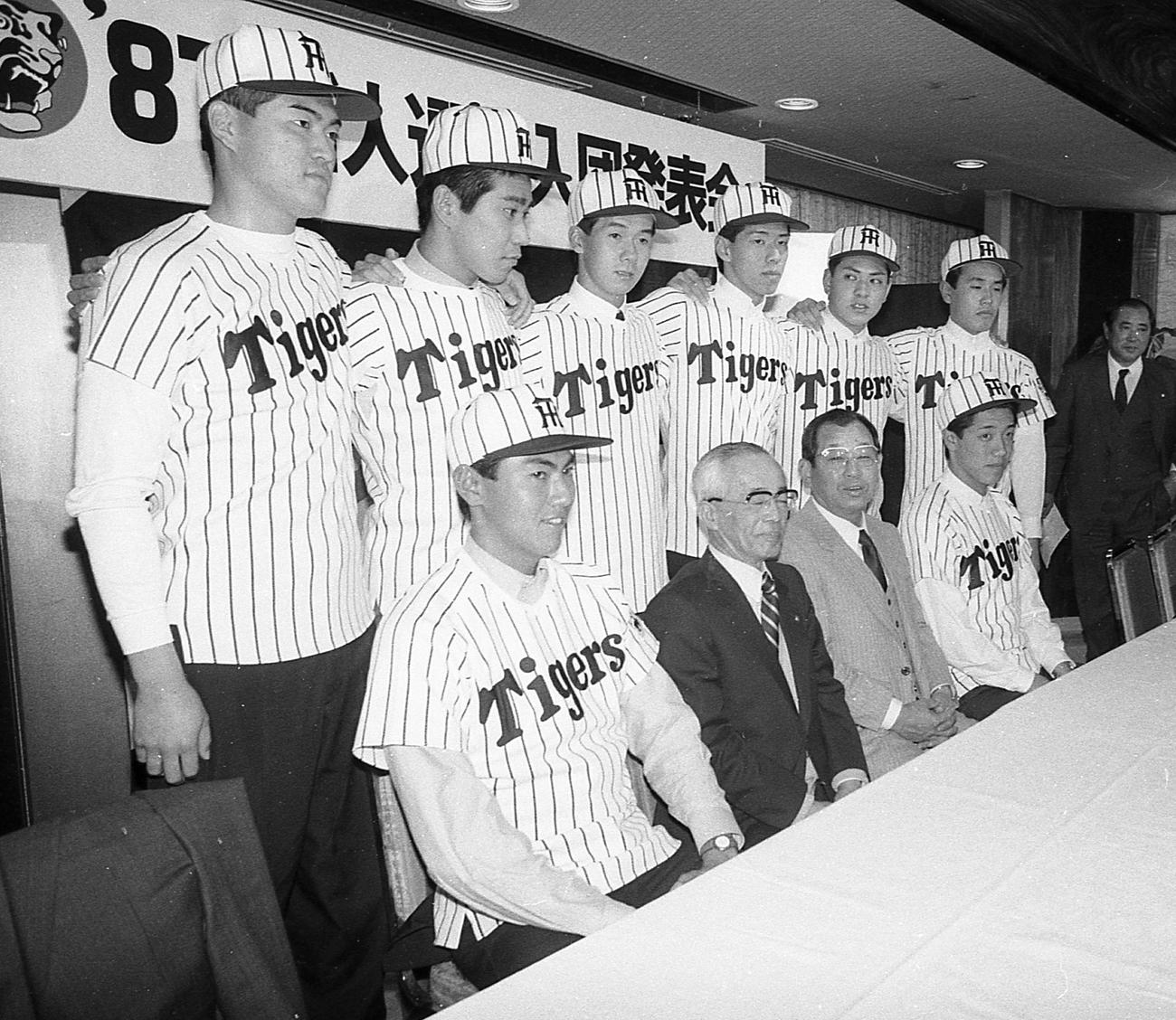 1987年度阪神新人入団発表に臨んだ真鍋勝已（後列右から2人目）、下段左から猪俣隆、岡崎社長、吉田義男監督、嶋尾康史。後列左から、西里幸喜、高橋昌也、八木裕、多岐篤司、ひとりおいて坂孝一