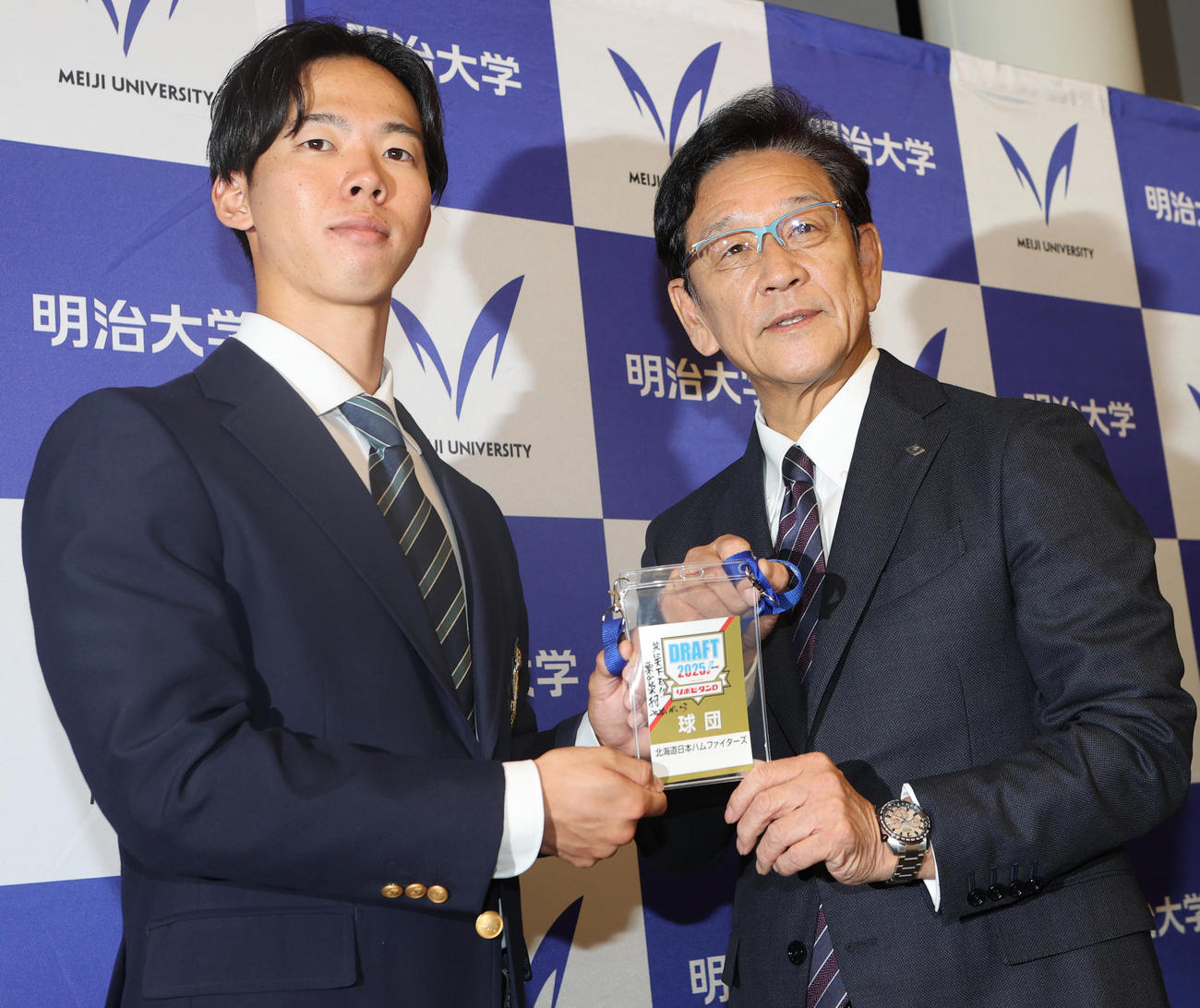 あいさつに訪れた日本ハム栗山CBO（右）からドラフト会議で使用したIDを渡される日本ハムドラフト1位の明大・大川（撮影・水谷安孝）