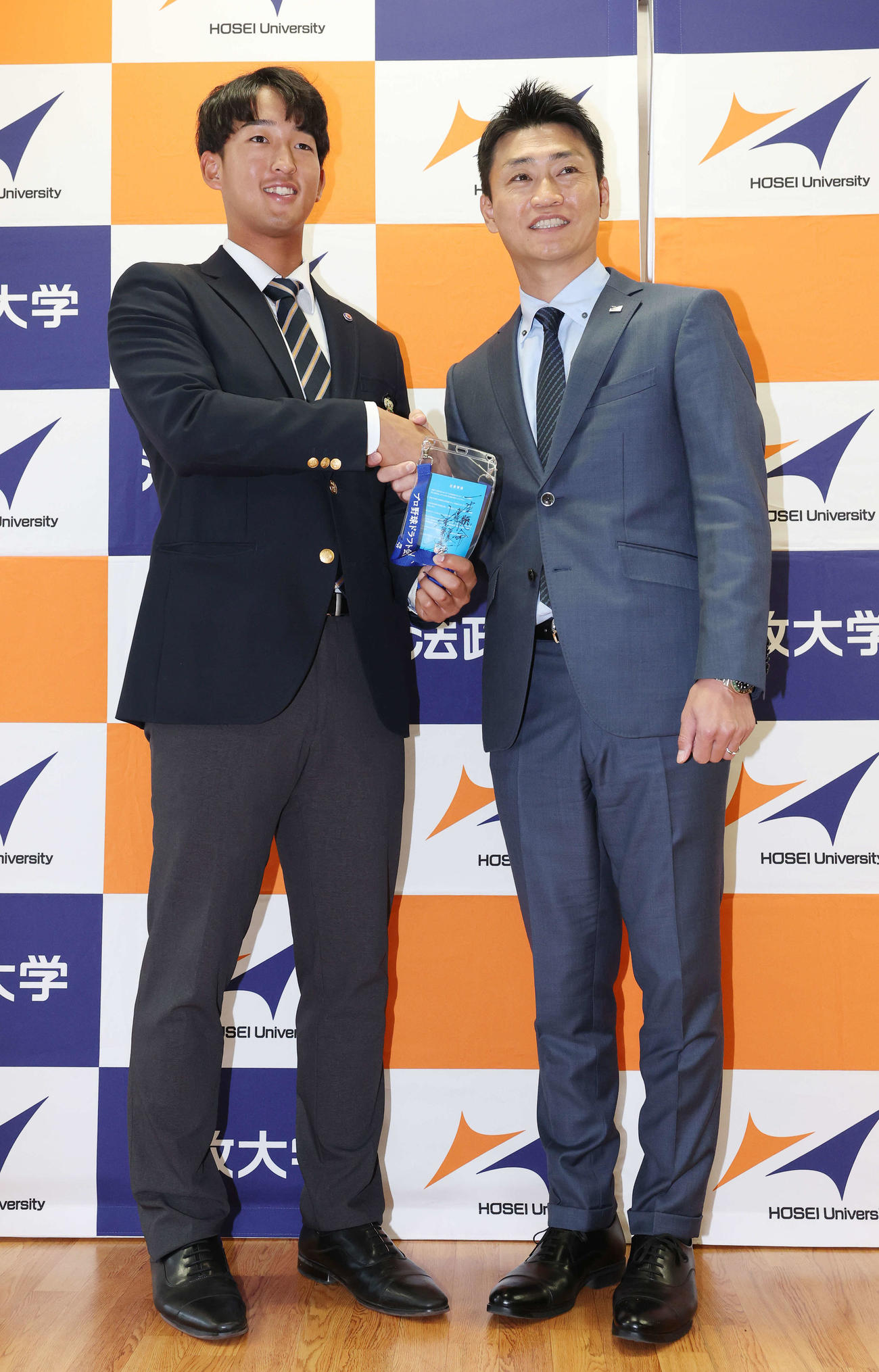 指名あいさつを受け、ヤクルト池山監督の直筆メッセージ入りパスを手に青木GM特別補佐（右）と笑顔で握手するドラフト1位の法大・松下（撮影・宮地輝）