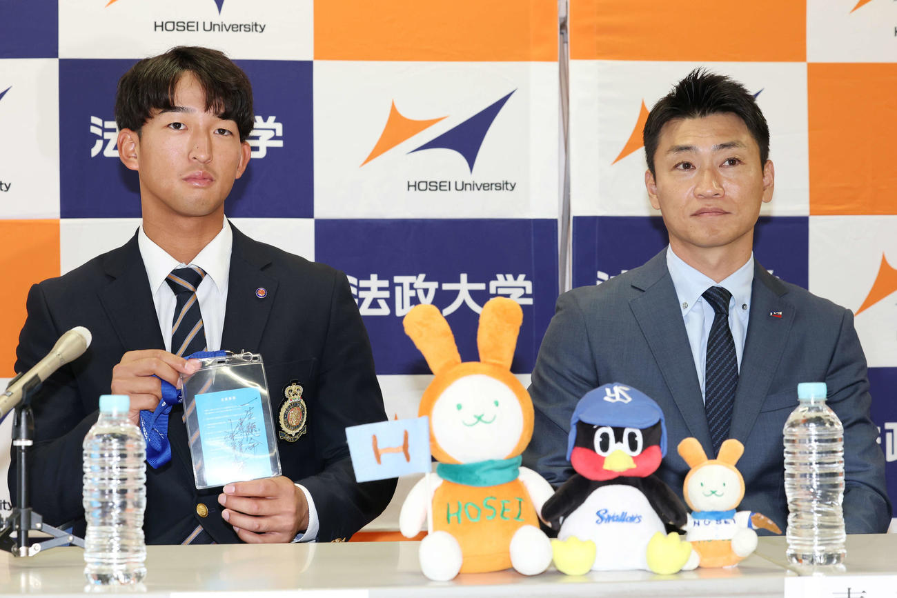 指名あいさつを受け、ヤクルト池山監督の直筆メッセージ入りパスを青木GM特別補佐（右）から受け取ったドラフト1位の法大・松下（撮影・宮地輝）