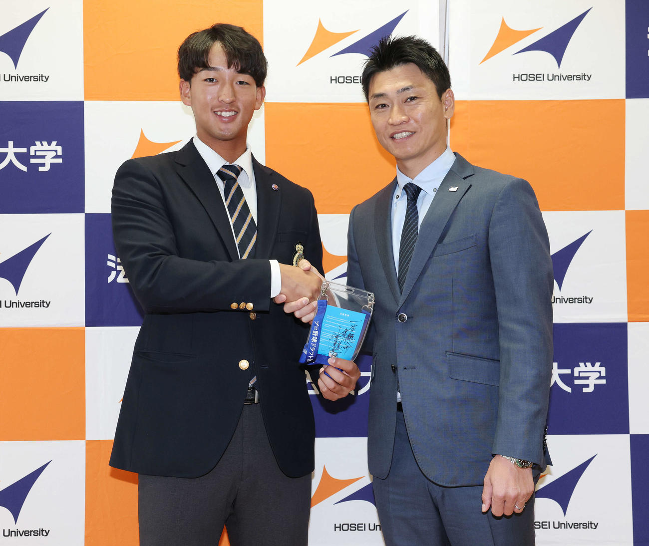 指名あいさつを受け、ヤクルト池山監督の直筆メッセージ入りパスを手に青木GM特別補佐（右）と笑顔で握手するドラフト1位の法大・松下（撮影・宮地輝）