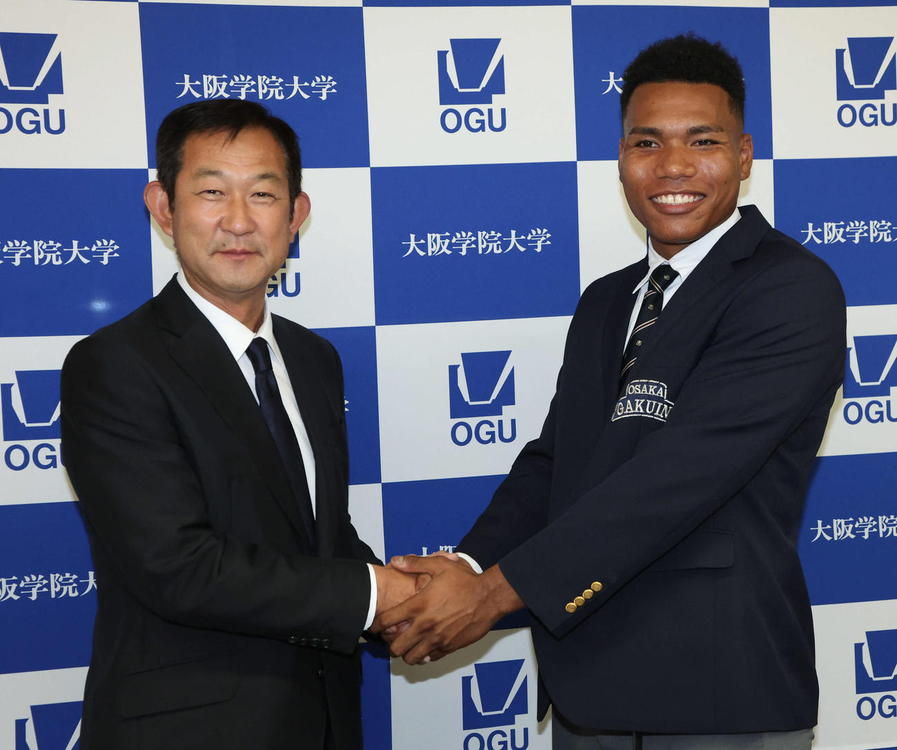 日本ハム2位の大阪学院大エドポロ　ケイン（右）は中村良二監督と握手をかわす（撮影・西尾就之）